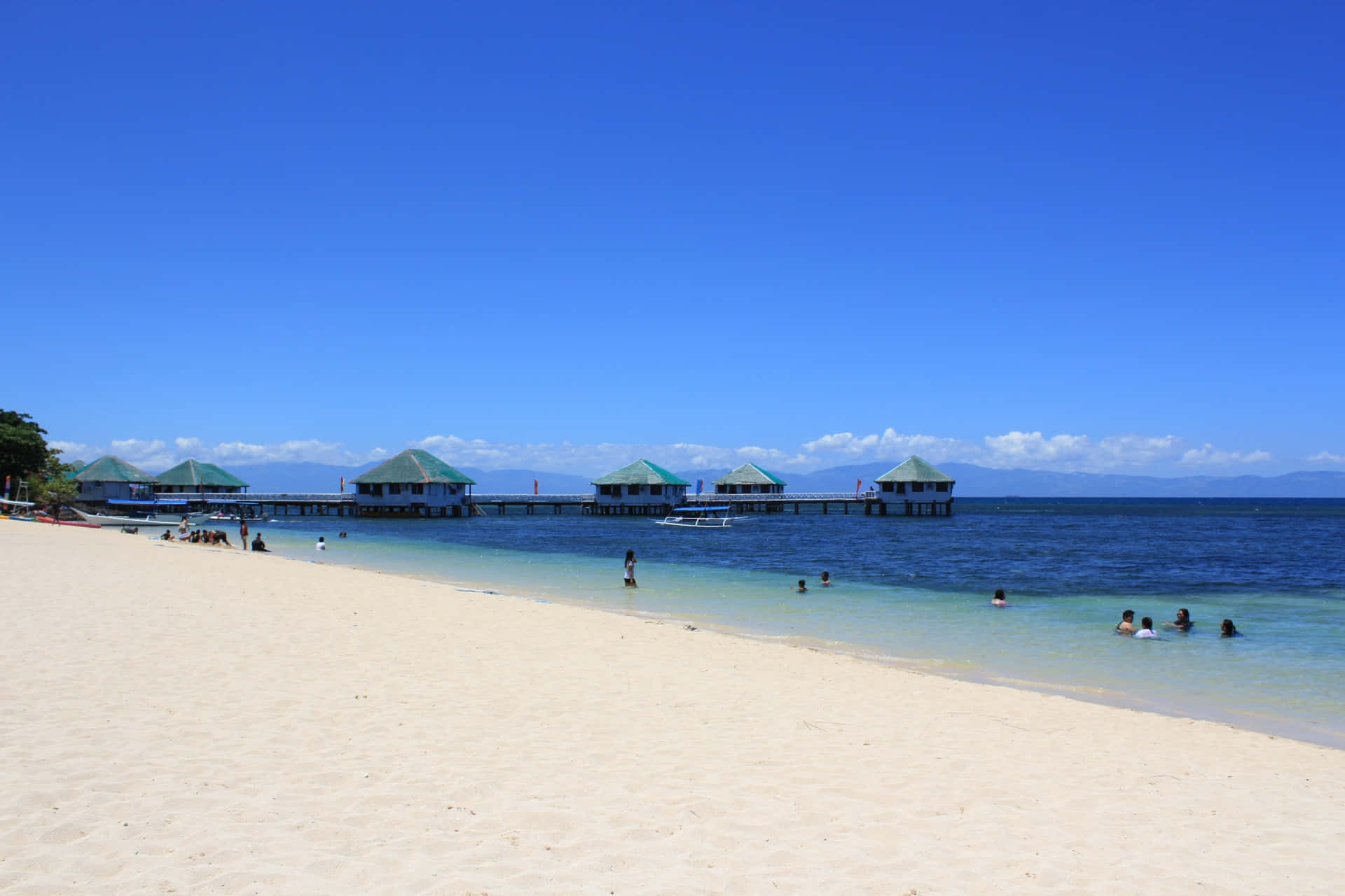 Beach Resort 桌布 壁紙 — 清澈藍天下，純白沙灘、碧綠海水和水上平房。