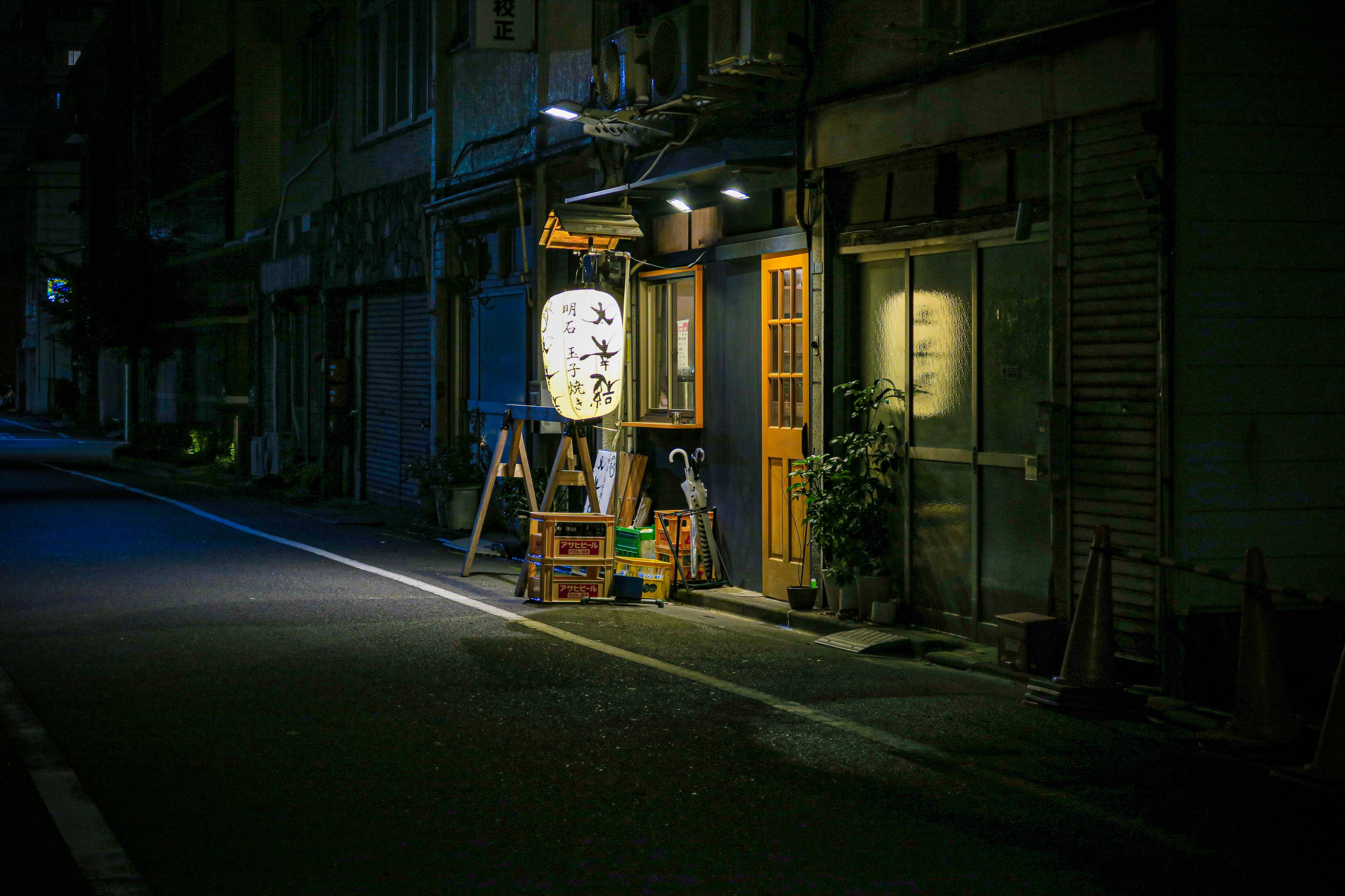 日本高畫質東京夜間燈籠 壁紙 — 夜晚一條寧靜的日本街道，被溫暖的燈籠和商店燈光照亮，在濕漉漉的人行道上投下長長的影子。