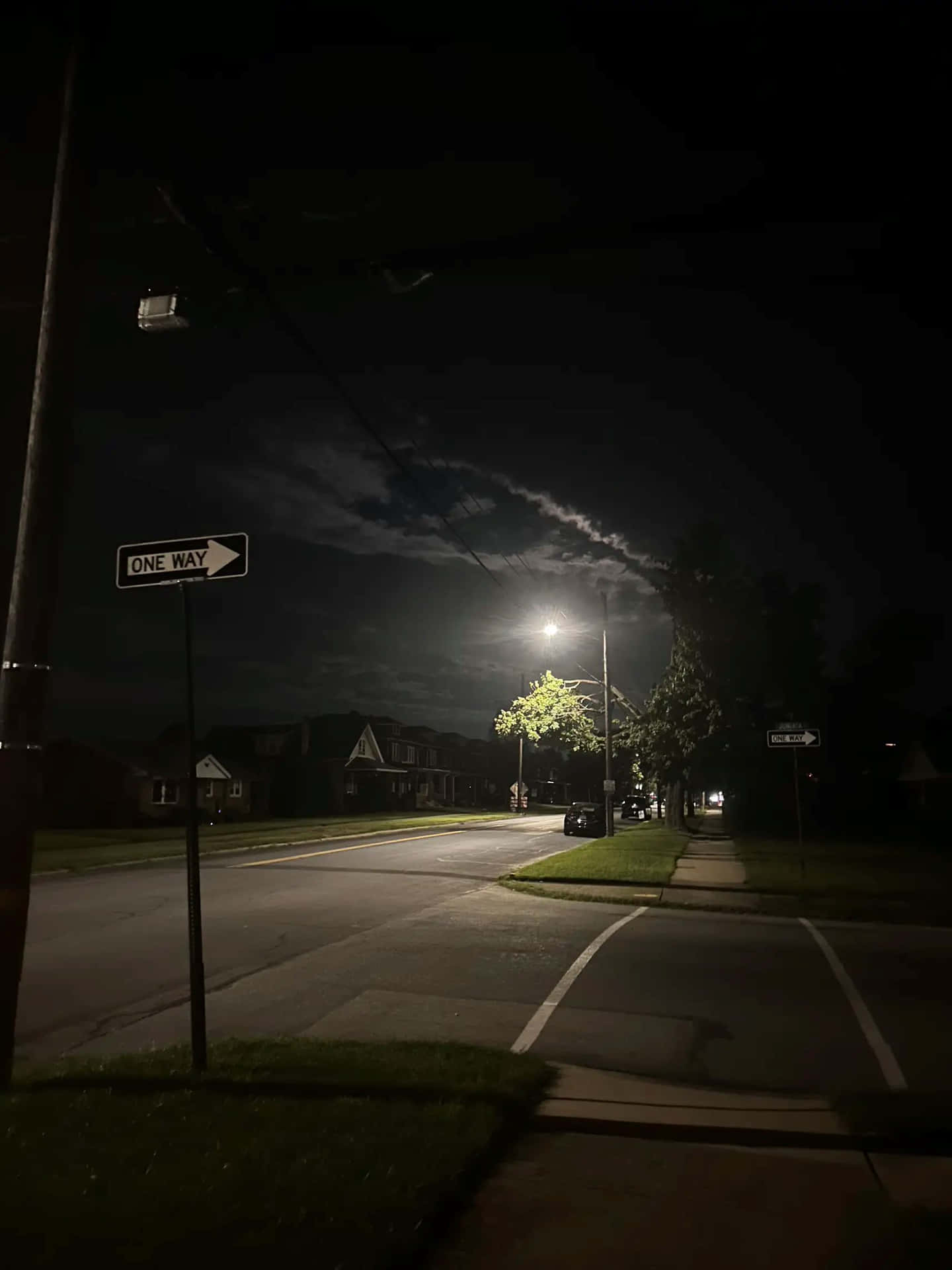  壁紙 — 一條寧靜的郊區街道在夜晚被一盞路燈照亮，燈光灑在樹木和房屋上，天空陰暗多雲。