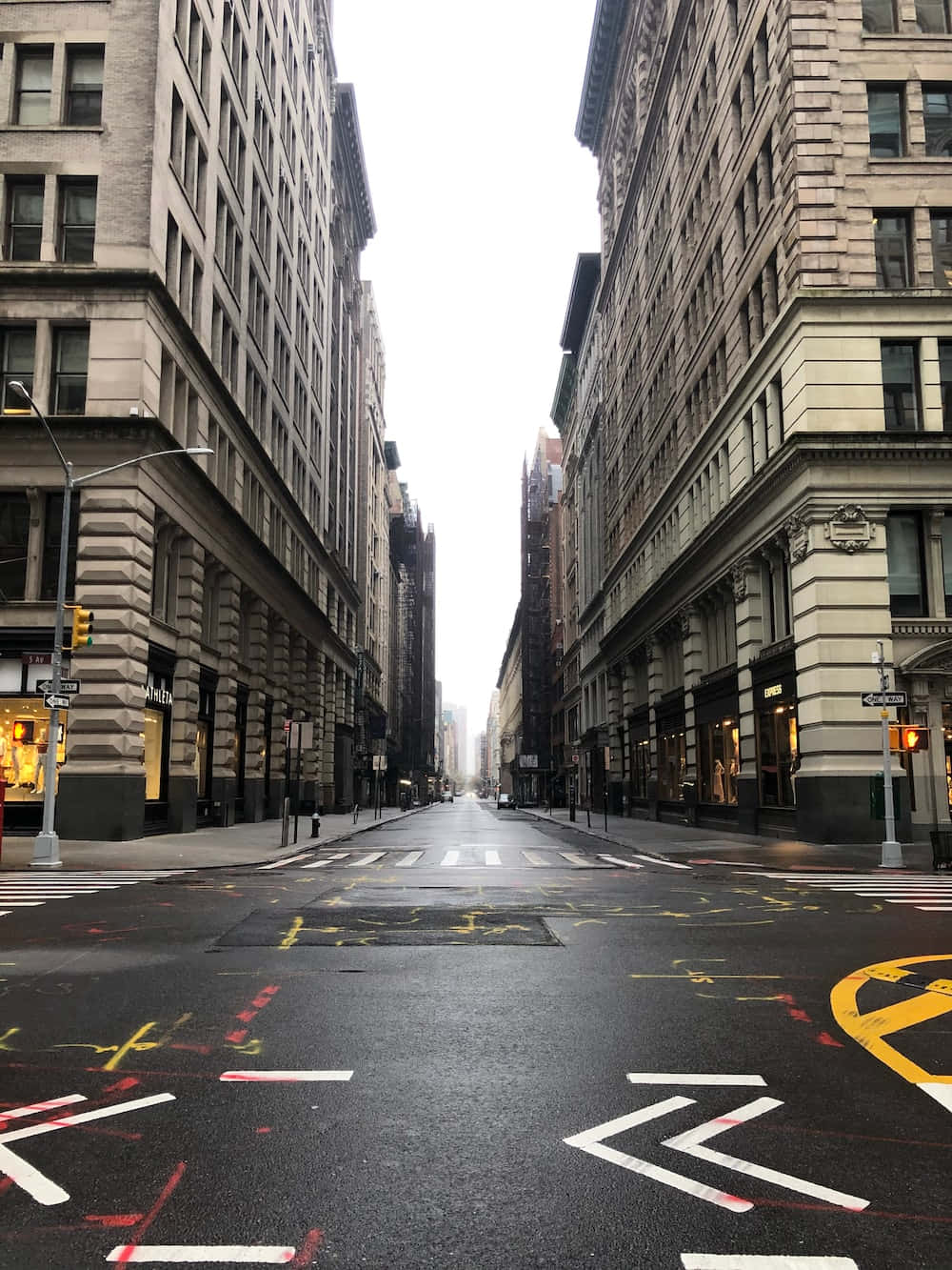 灰色天空下，空蕩的城市街道，高樓大廈和褪色的道路標記。