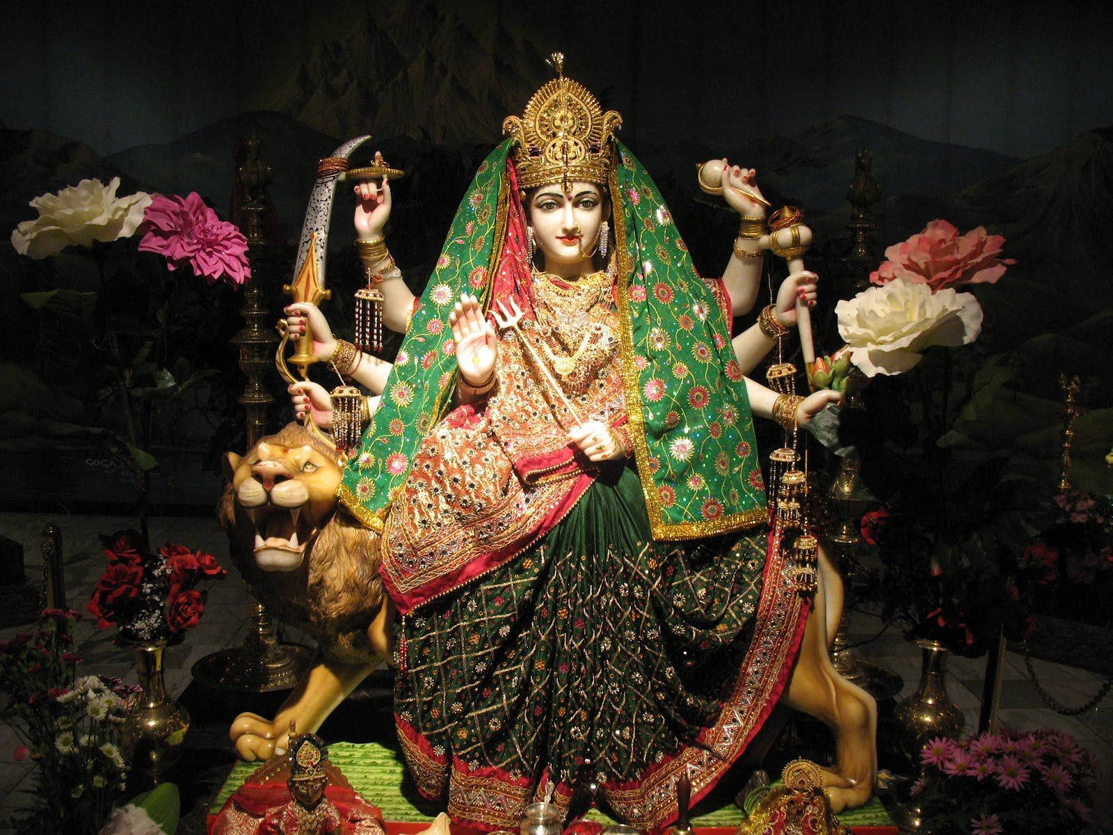 一尊印度教女神雕像，有多隻手臂和武器，騎著獅子，周圍環繞著花朵。
