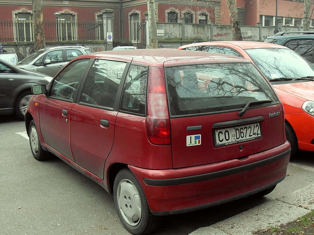 Fiat Punto 桌布 壁紙 — 一輛紅色Fiat Panda停泊在城市的街道上，背景有光禿禿的樹木和磚砌建築。