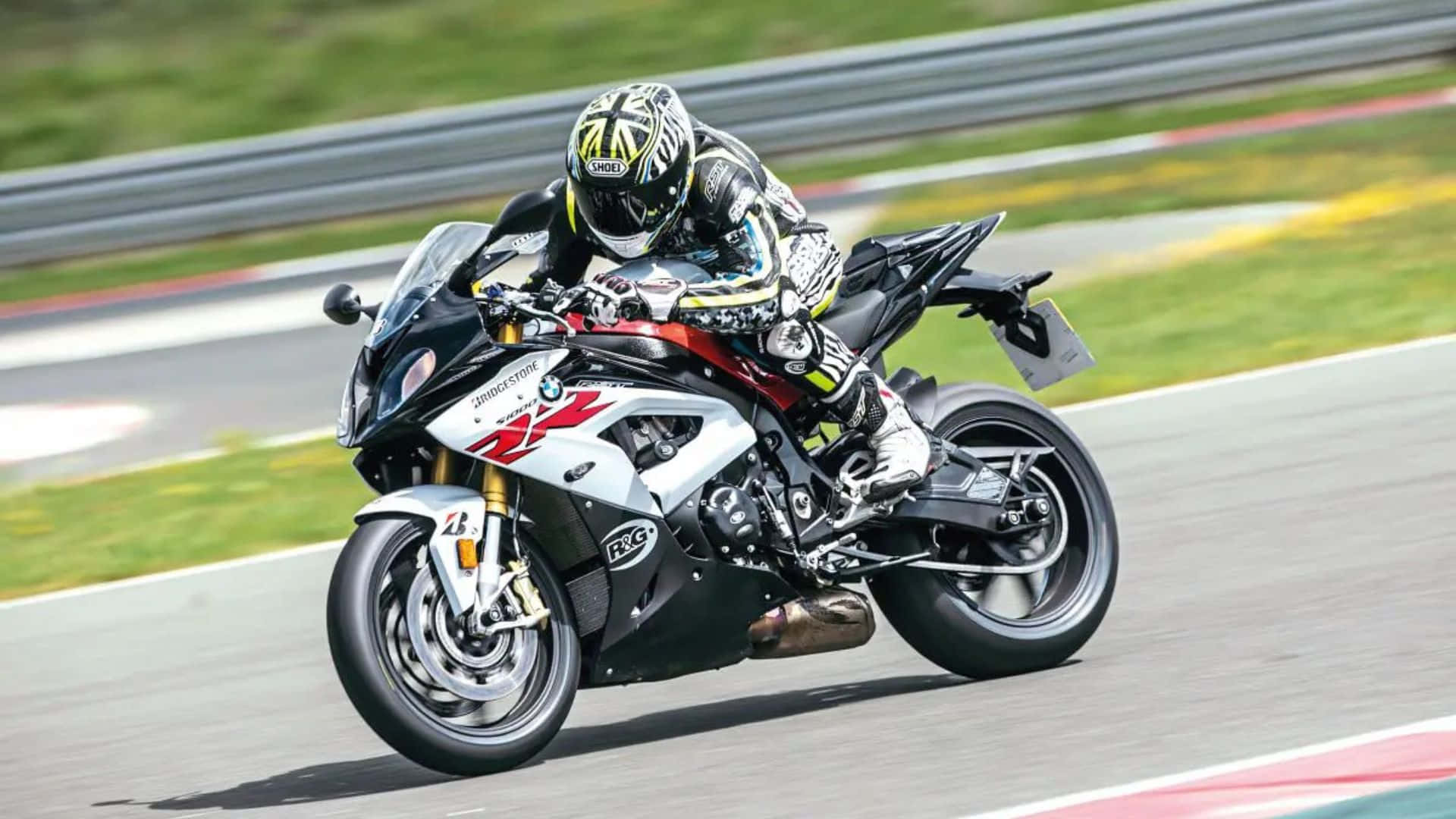  壁紙 — 一名騎手在陽光普照的賽道上，騎著白色和黑色的BMW S1000RR電單車，傾斜入彎，背景有模糊的綠色草地和護欄。