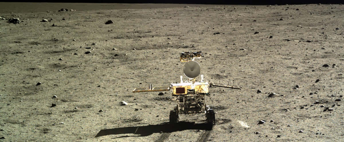 Lunar Rover 桌布 壁紙 — 一個帶有碟形天線的機械人探測車站在荒蕪的灰色月球表面，點綴著岩石，在明亮的陽光下。