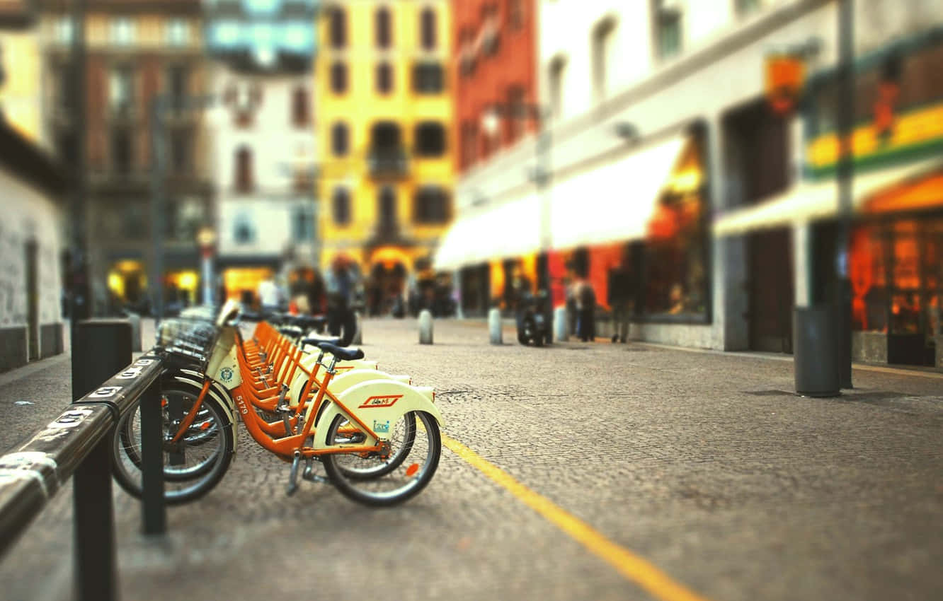 橙色租賃單車沿著鵝卵石街道停放，建築物模糊。