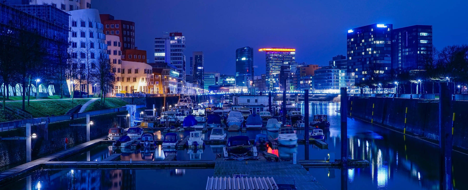 繁茂熱帶風光 壁紙 — 城市運河的寧靜夜景，停泊的船隻倒映著現代建築的霓虹燈光。