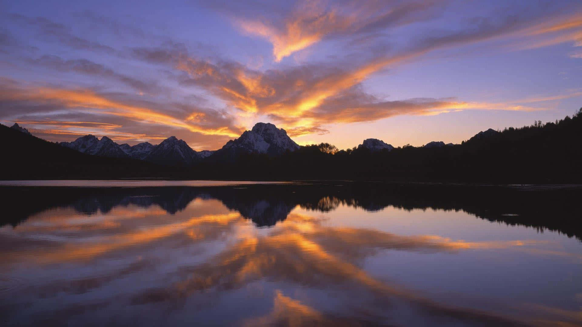 Sunset Reflection 桌布 壁紙 — 寧靜的日落映照在白雪覆蓋的山峰上，完美地倒映在平靜的湖面上，伴隨著鮮豔的橙色和紫色雲彩。