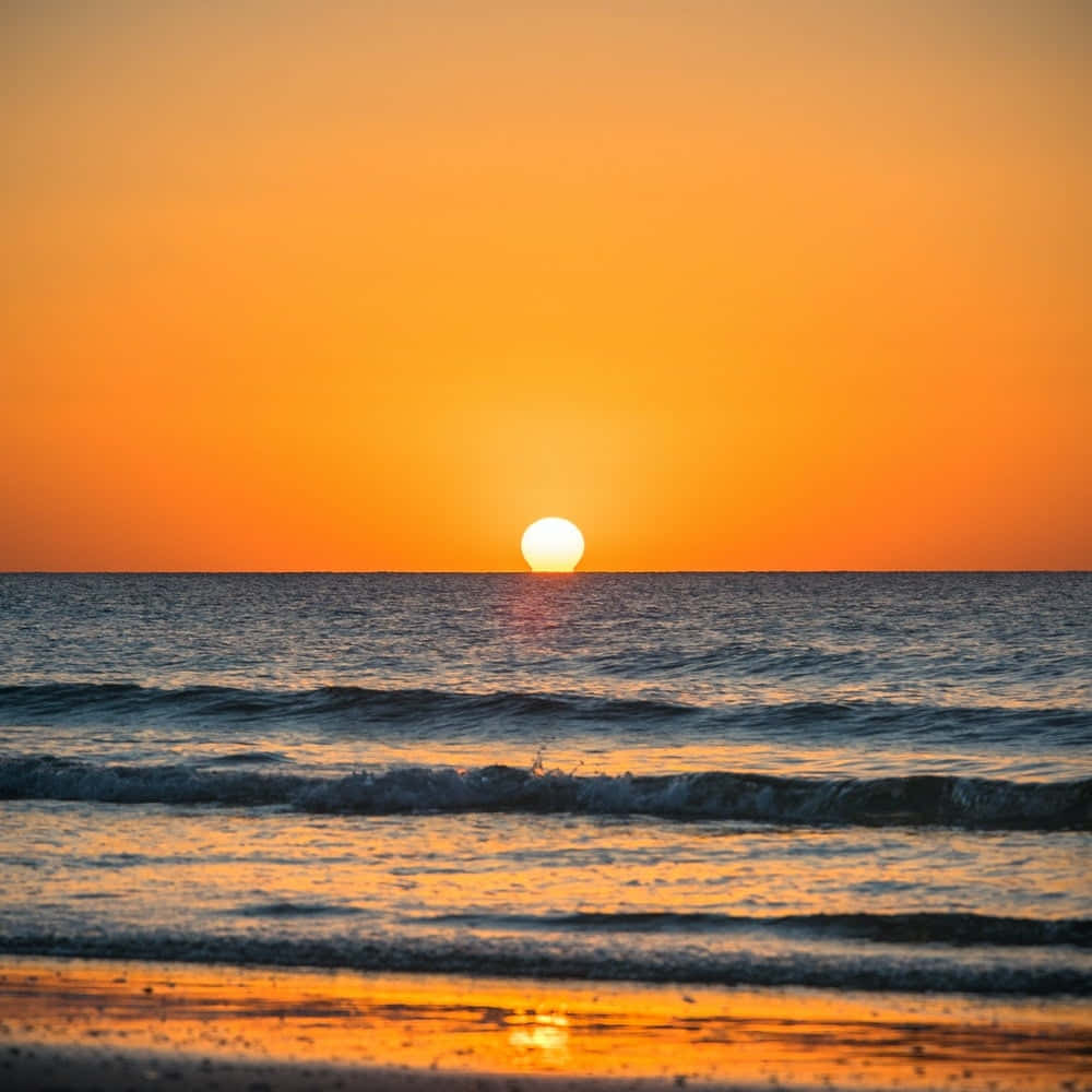 Sunset Photography 桌布 壁紙 — 寧靜的海洋日落，發光的太陽觸及地平線，波浪在濕沙上反射金色光芒。