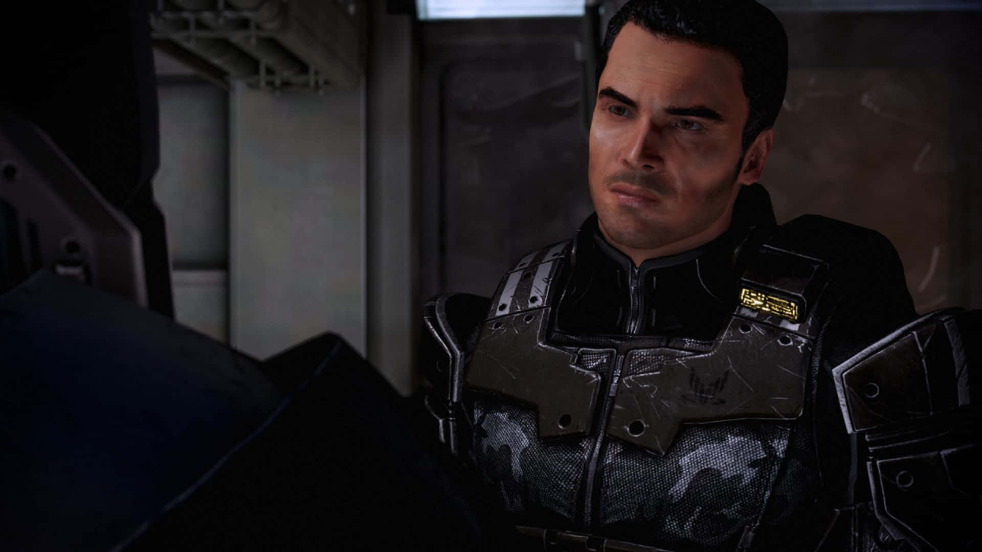 Kaidan Alenko 桌布 壁紙 — 一個嚴肅的男人穿著深色未來裝甲，站在昏暗的工業環境中，光線聚焦。
