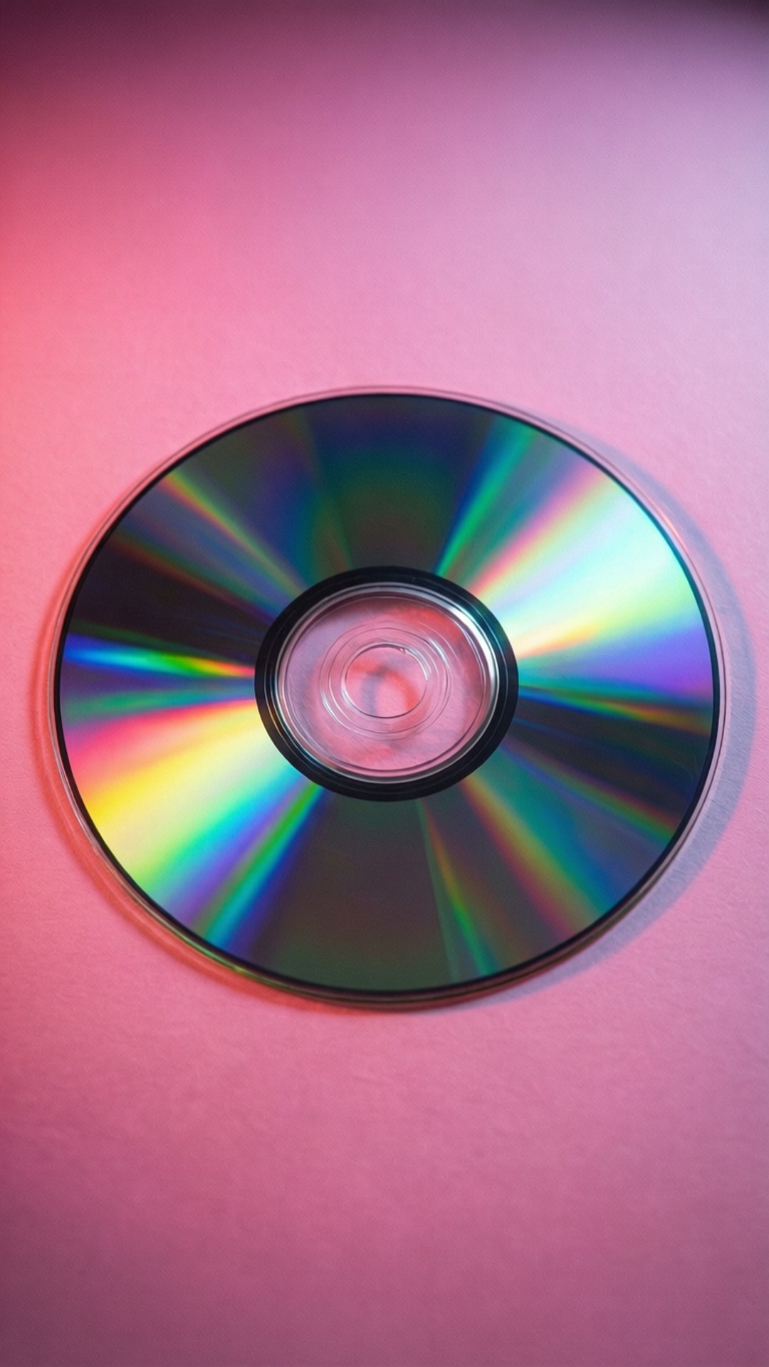 粉紅色表面上帶有彩虹光圖案的彩色CD。