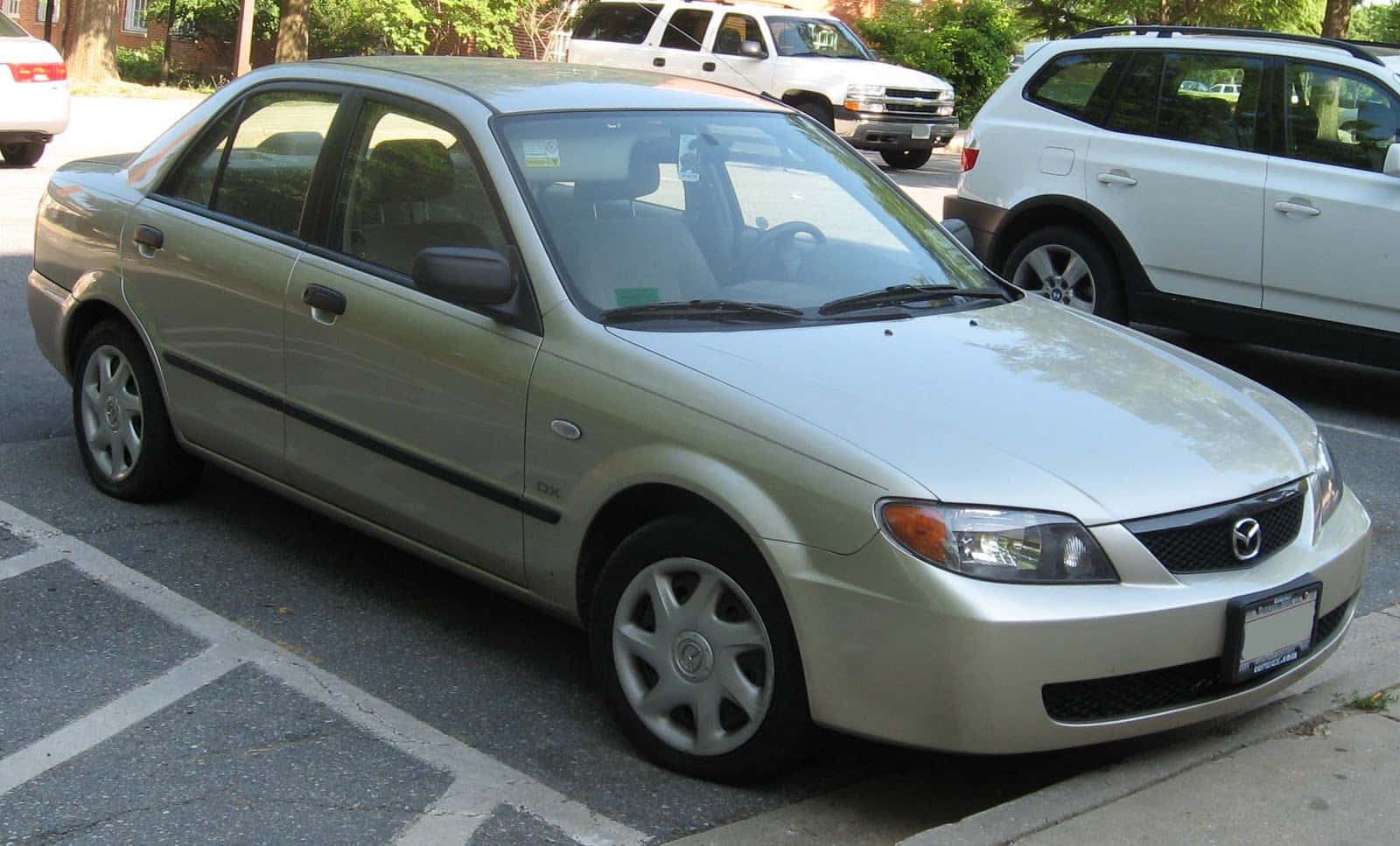 Mazda Protege 桌布 壁紙 — 一架銀色Mazda 626房車停泊在陽光普照的瀝青停車場，附近有其他車輛。