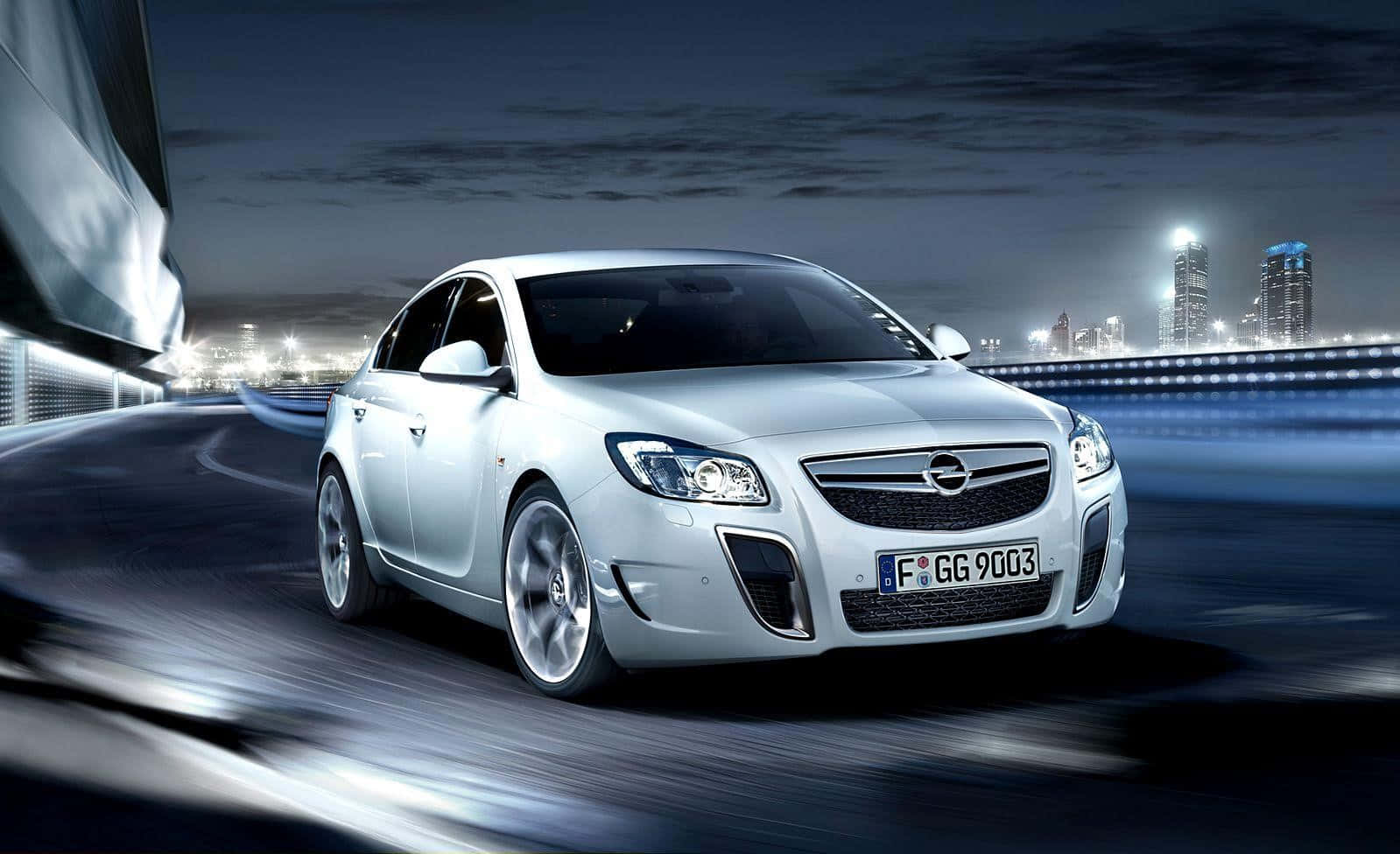 Opel Insignia 桌布 壁紙 — 一輛銀色Opel speedster在夜間行駛在濕漉漉的城市道路上，背景有模糊的燈光和發光的摩天大樓。