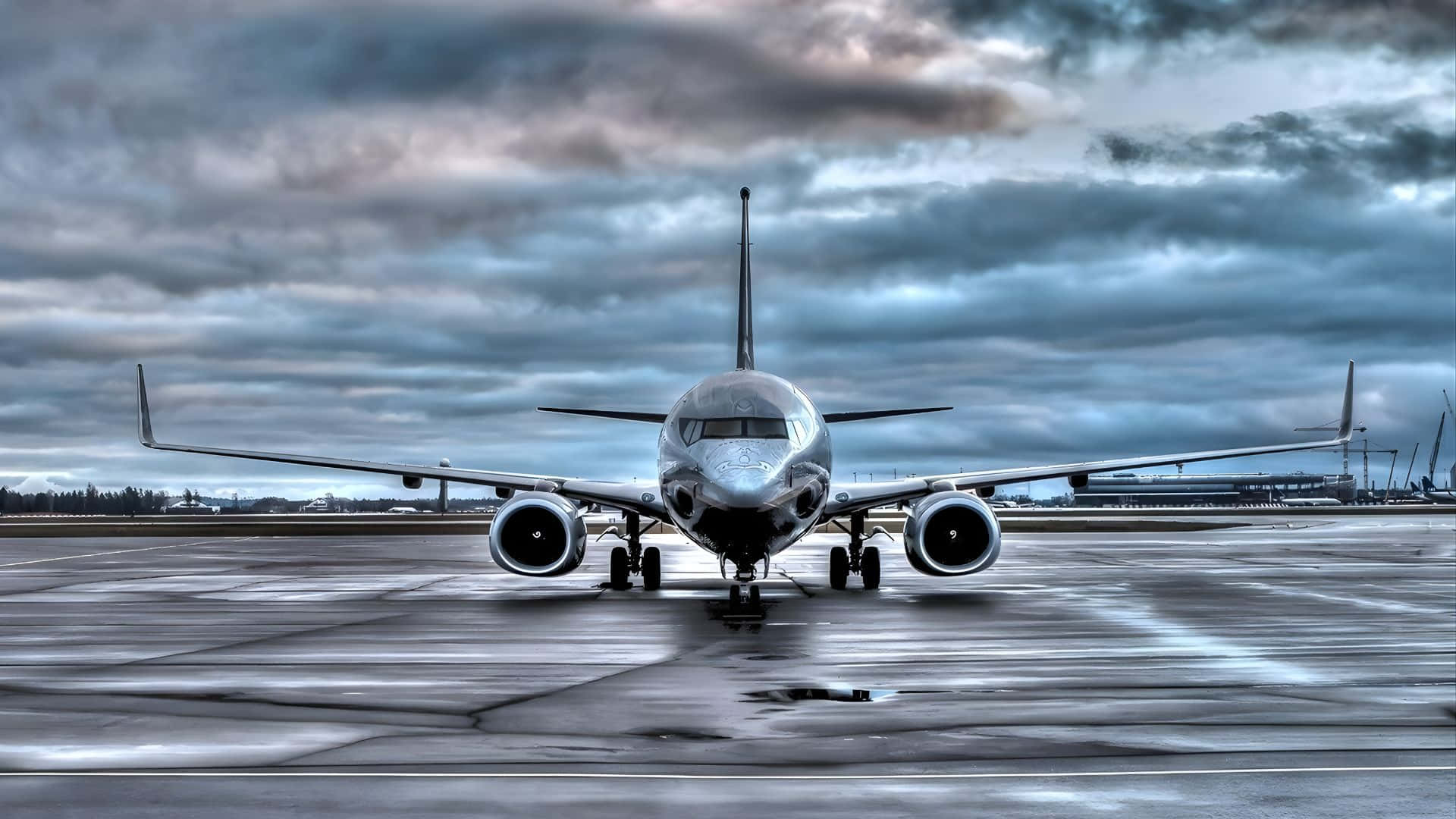  壁紙 — 一架流線型飛機在濕滑停機坪上向前，背景是戲劇性的多雲天空和遠處的機場建築。