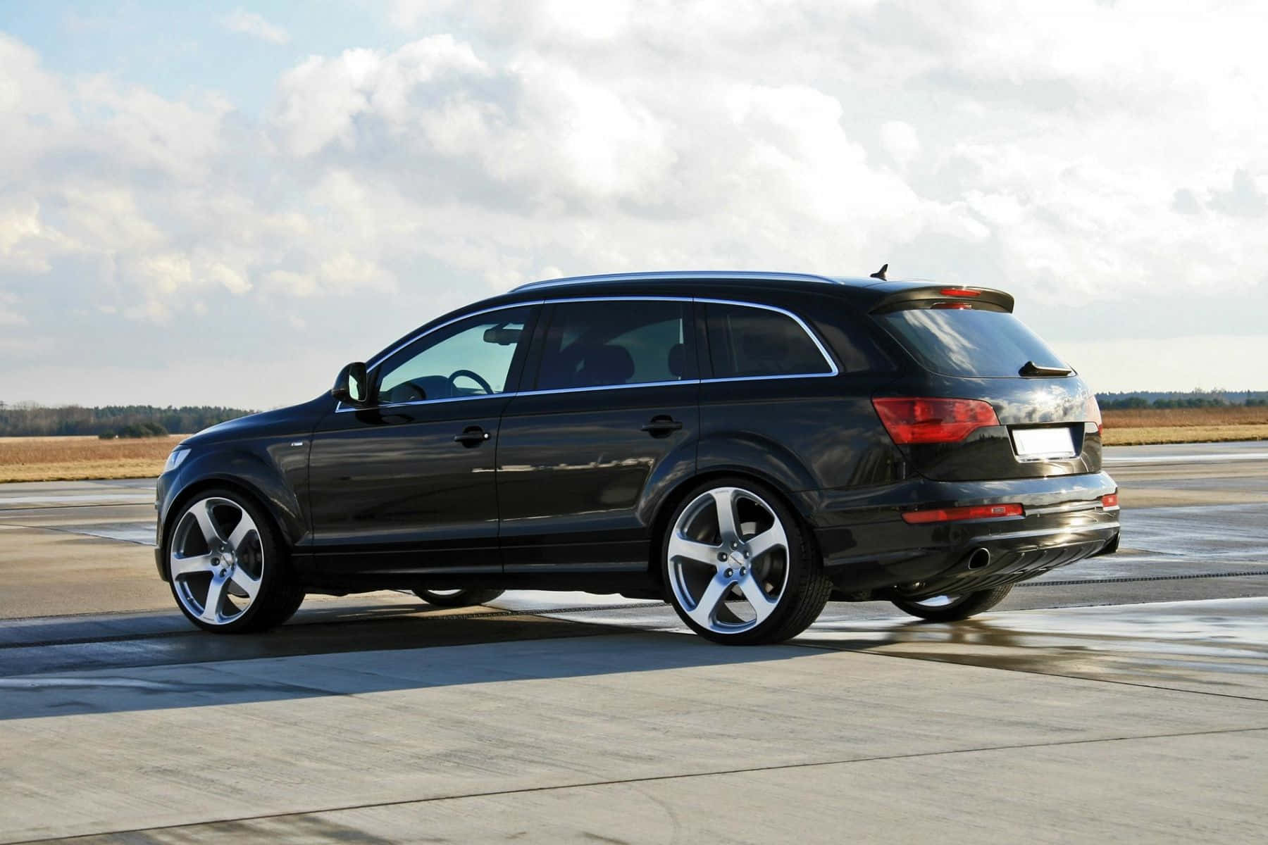 Audi Q7 桌布 壁紙 — 一輛時尚的黑色奧迪Q7 SUV停泊在潮濕的停機坪上，天空多雲，遠處有樹木。