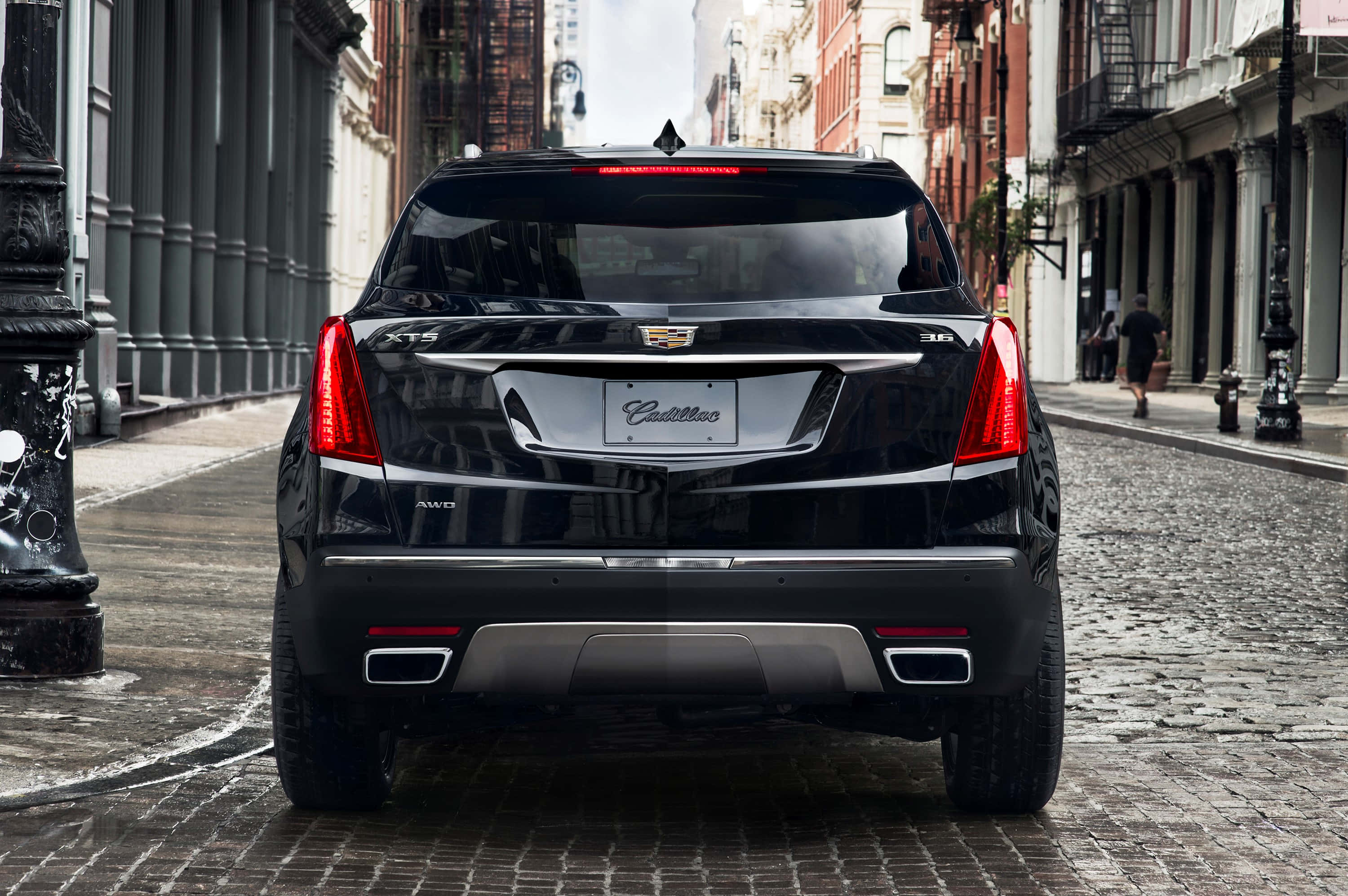 Cadillac Xt5 桌布 壁紙 — 一輛時尚的黑色凱迪拉克SUV停在濕漉漉的鵝卵石街道上，兩旁是歷史悠久的磚砌建築。