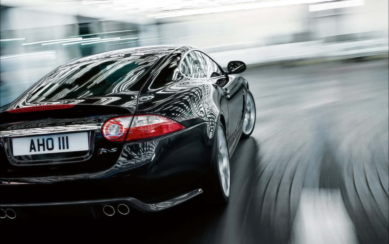 Jaguar Xkr 桌布 壁紙 — 一輛時尚的黑色積架跑車在模糊的城市隧道中疾馳，動態模糊強調了速度。