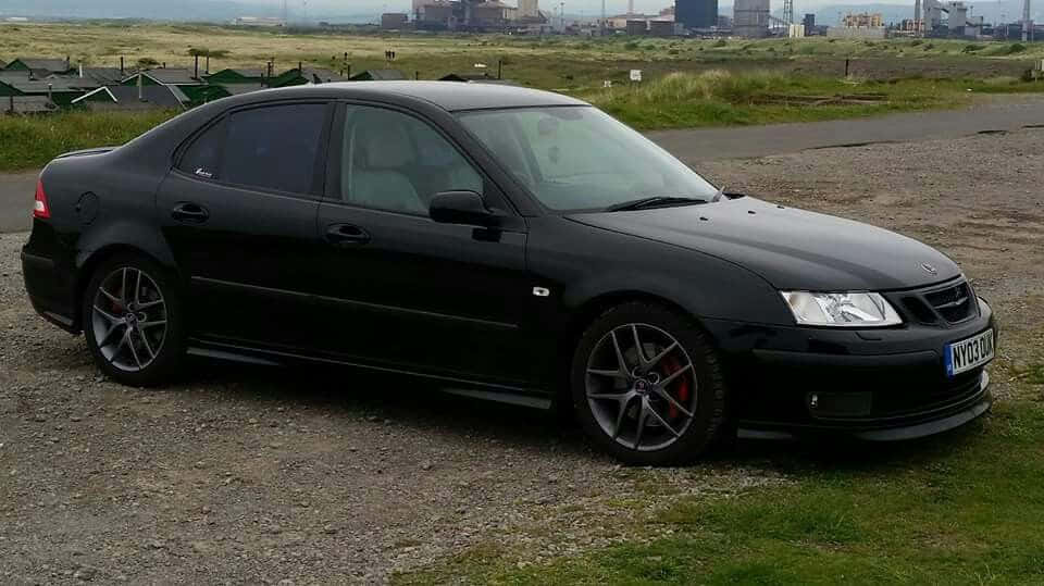 Saab 99 桌布 壁紙 — 一架型格黑色Saab 9-3運動房車停泊在碎石路上，遠方朦朧可見工業建築。