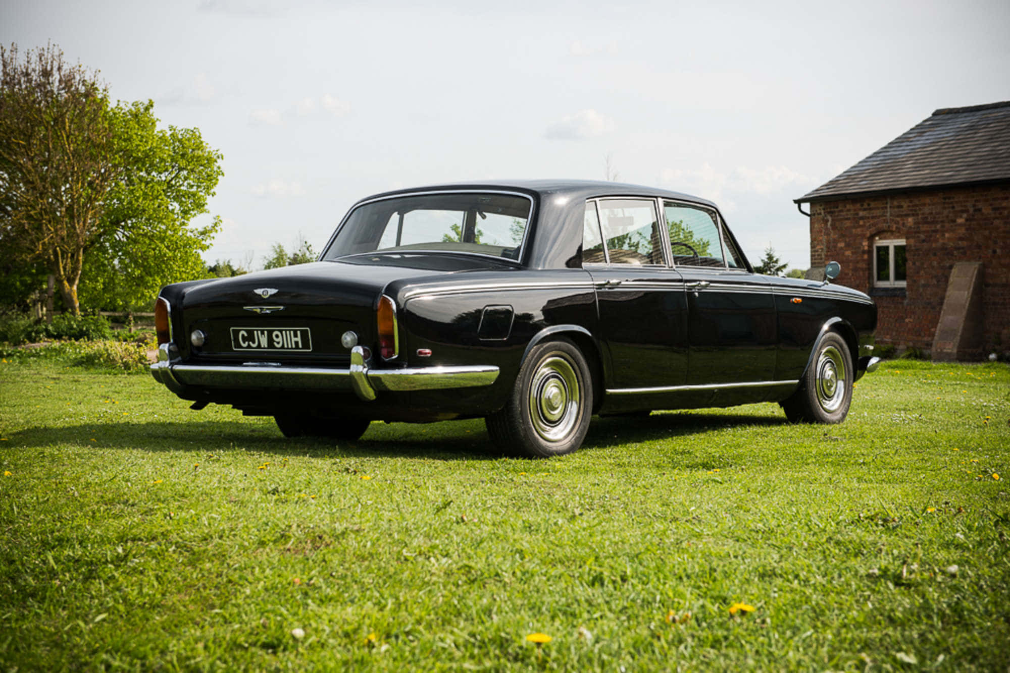 Bentley T1 桌布 壁紙 — 一輛時尚的黑色復古車在陽光明媚的草地上閃閃發光，旁邊是一座磚砌建築，背景有樹木。