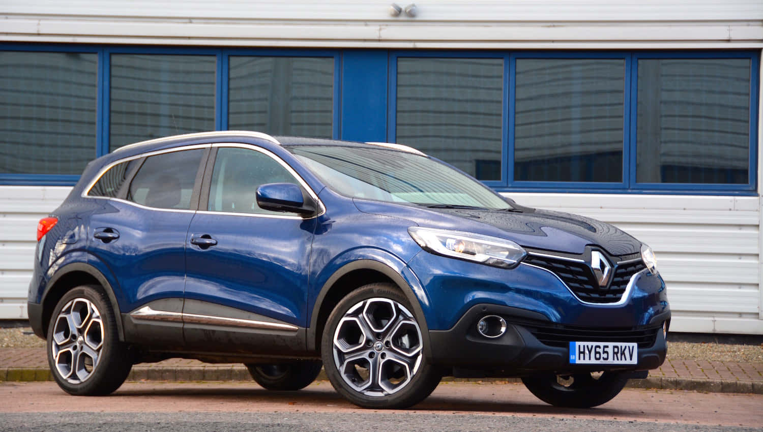  壁紙 — 一輛時尚的藍色雷諾 Captur SUV 停在現代建築前，建築物帶有藍色框架的窗戶。