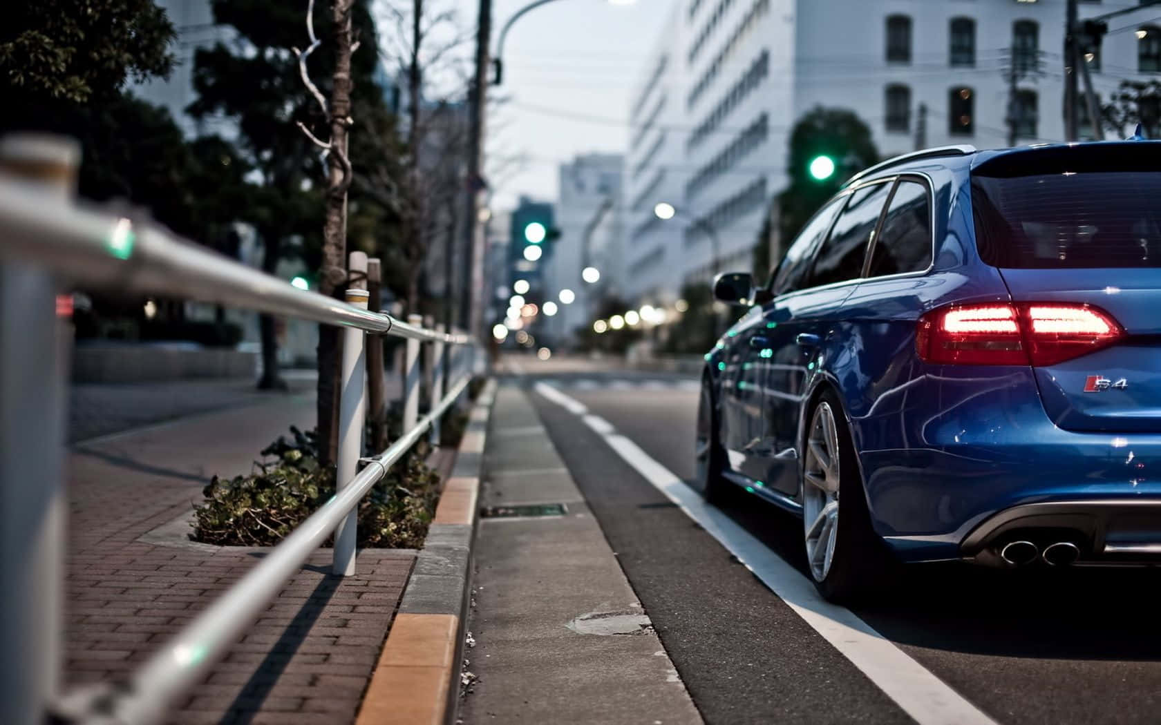 Audi S4 桌布 壁紙 — 一輛時尚的藍色旅行車在黃昏時停泊在城市街道上，帶有發光的尾燈和模糊的城市背景。