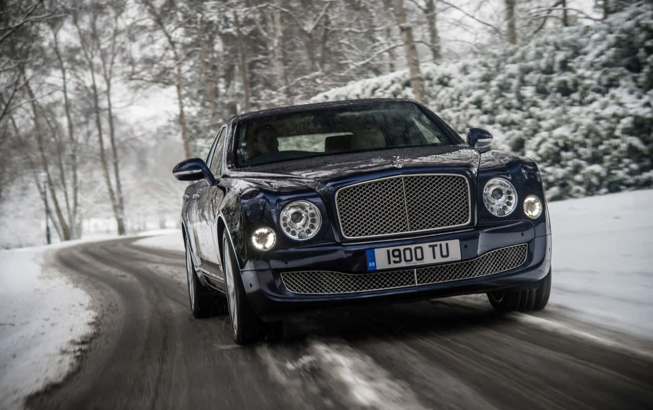 Bentley Mulsanne 桌布 壁紙 — 一輛時尚的深藍色賓利 Bentayga 在冬季自信地行駛在一條白雪覆蓋的森林道路上，兩旁是光禿的樹木和常青樹。