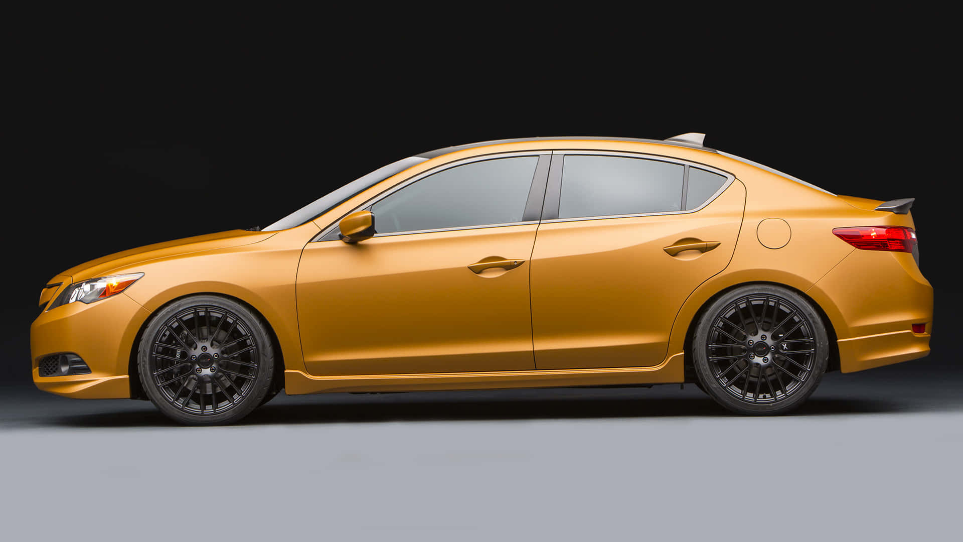 Acura Ilx 桌布 壁紙 — 一輛時尚的黃金轎車配黑色輪圈，在黑暗的攝影棚背景下側面展示。