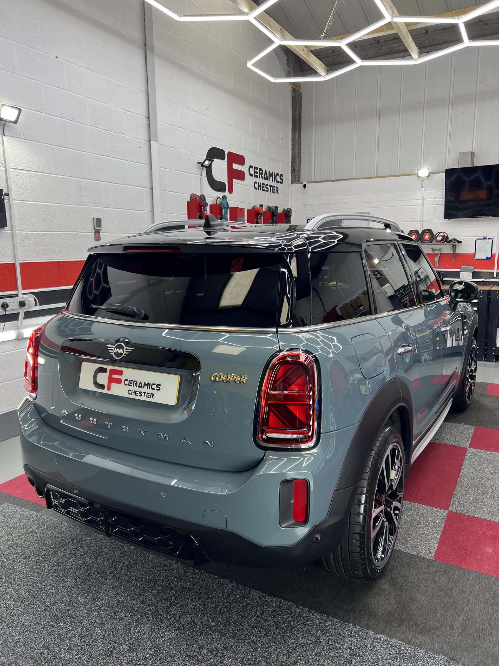 Mini Cooper Countryman 桌布 壁紙 — 一架時尚的灰色MINI Countryman Cooper停泊在室內，地面是紅灰格子地板，上方是現代六角形燈光。