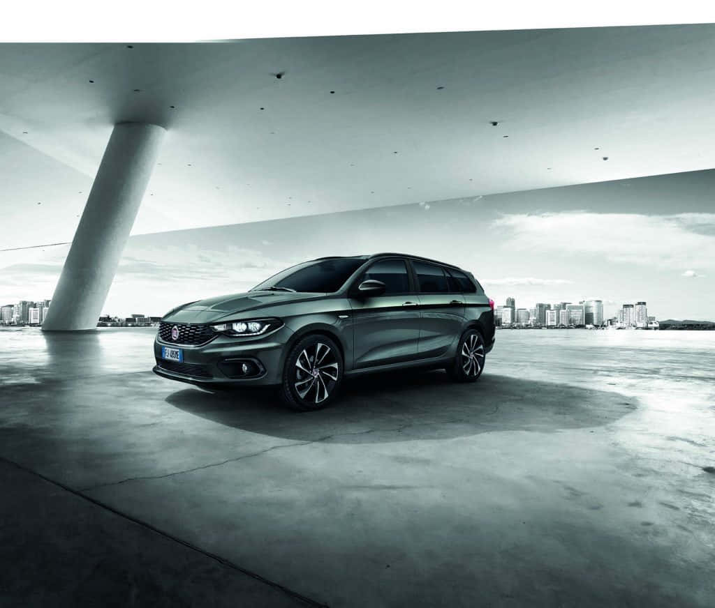 Fiat Tipo 桌布 壁紙 — 一架時尚的灰色旅行車停泊在現代混凝土天橋下，背景是城市天際線。