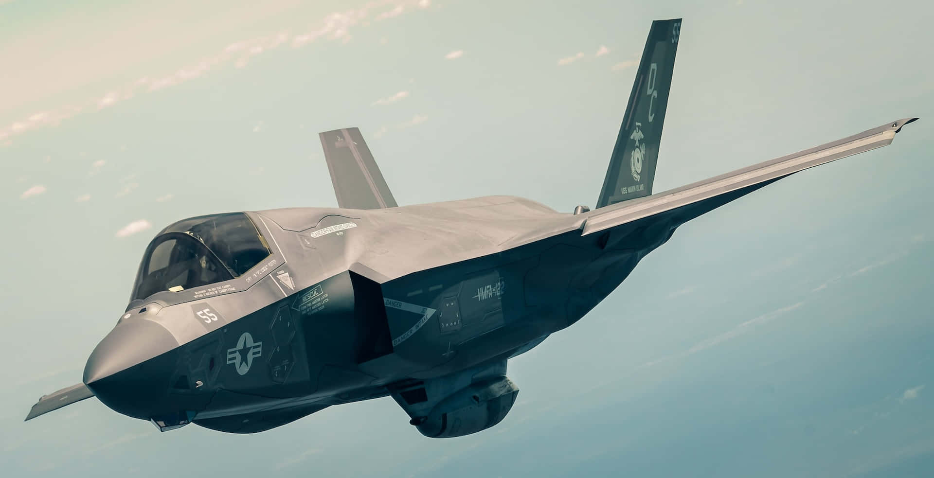  壁紙 — 一架流線型灰色隱形戰鬥機在淡藍色天空翱翔，下方有縷縷白雲。