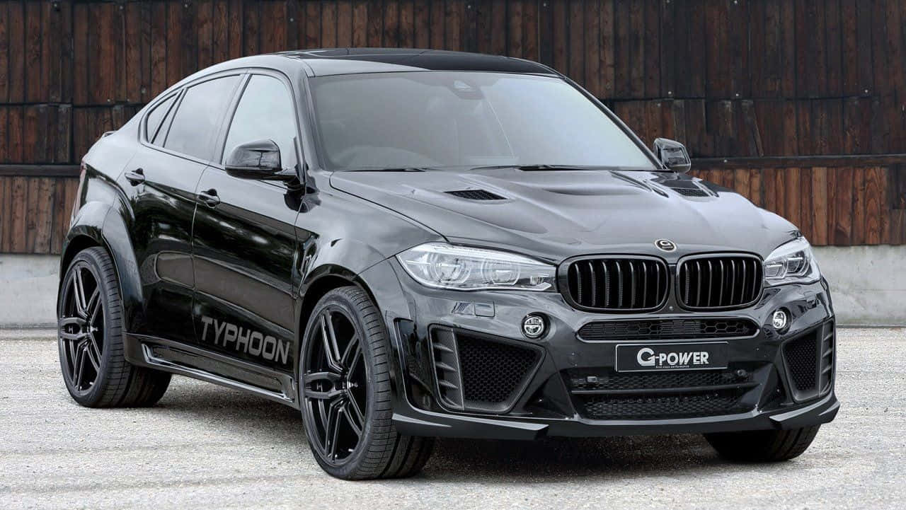 Bmw X6 桌布 壁紙 — 一輛時尚的啞光黑色G-Power Typhoon BMW X6M停泊在碎石上，背景是木柵欄。