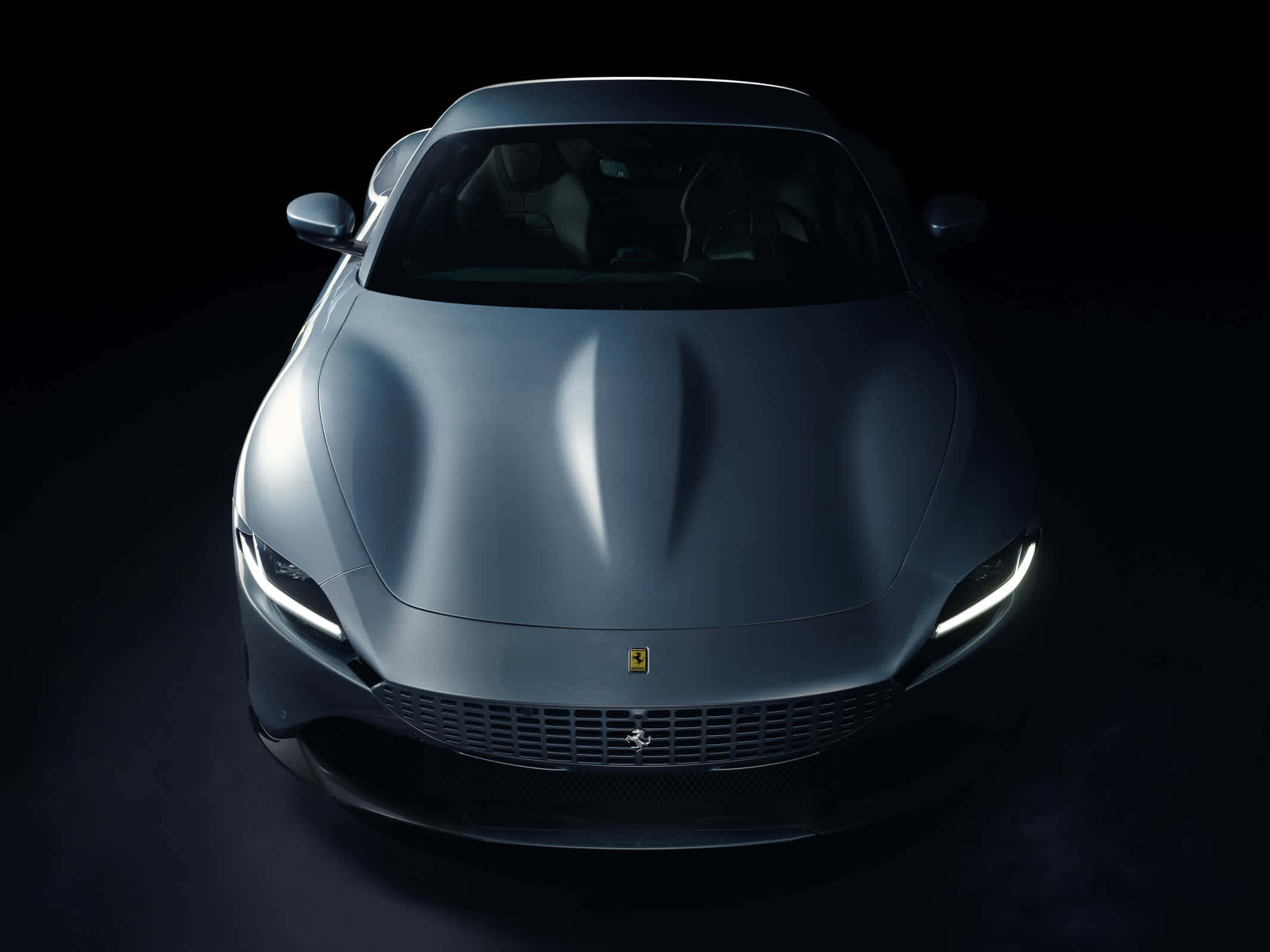 Ferrari Roma 桌布 壁紙 — 一輛時尚的啞光灰色法拉利跑車在黑色背景下的戲劇性工作室燈光中閃耀。