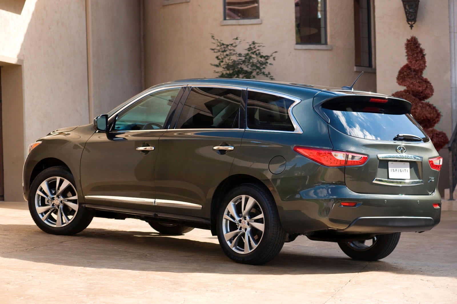 Infiniti Jx35 桌布 壁紙 — 一架時尚嘅橄欖綠色 Infiniti QX70 SUV 停泊喺米色灰泥建築前面，喺明亮嘅日光下。