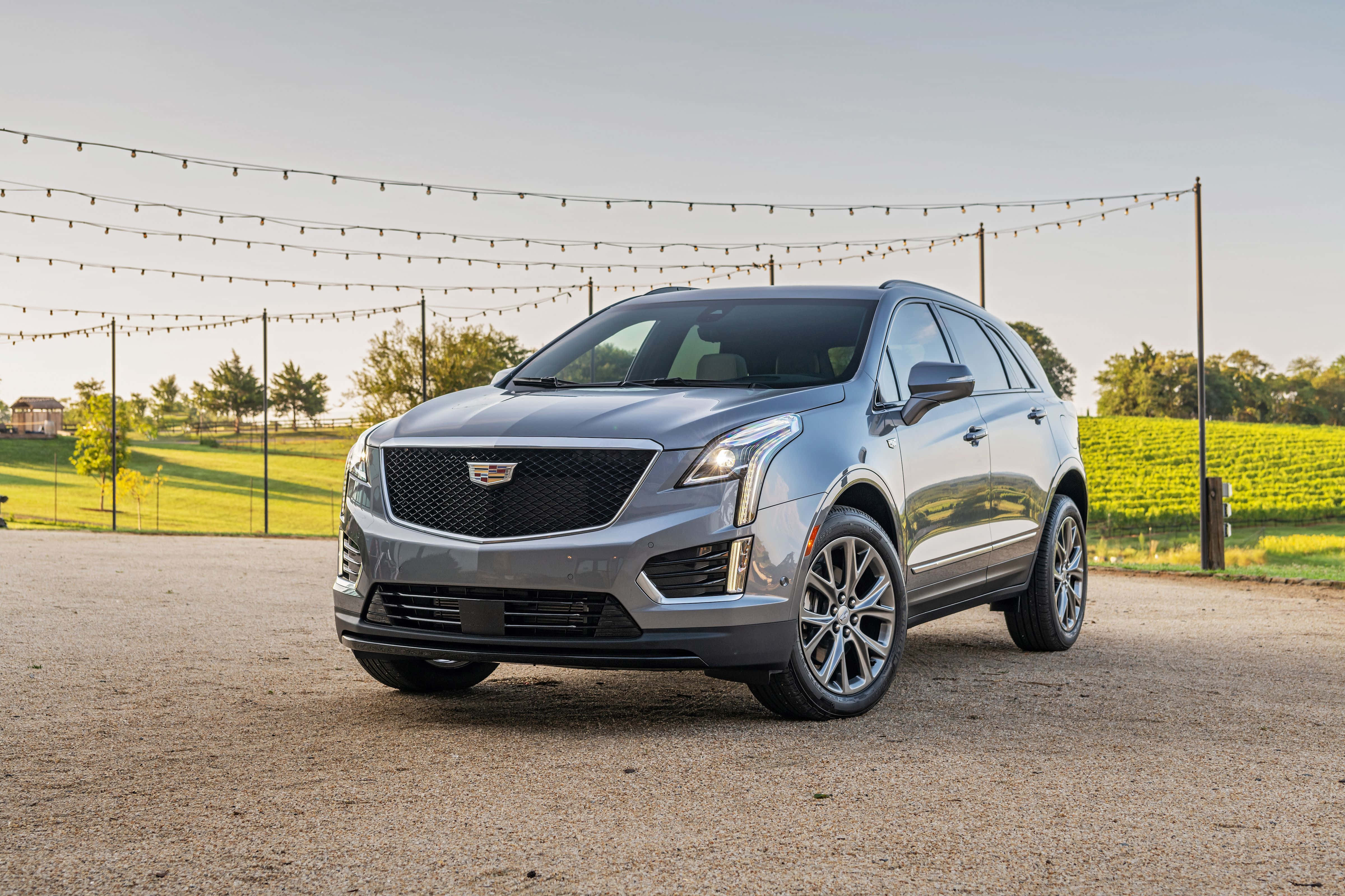 Cadillac Xt5 桌布 壁紙 — 一架時尚的銀色凱迪拉克SUV停在碎石上，頭頂有串燈，背景是綠色田野。