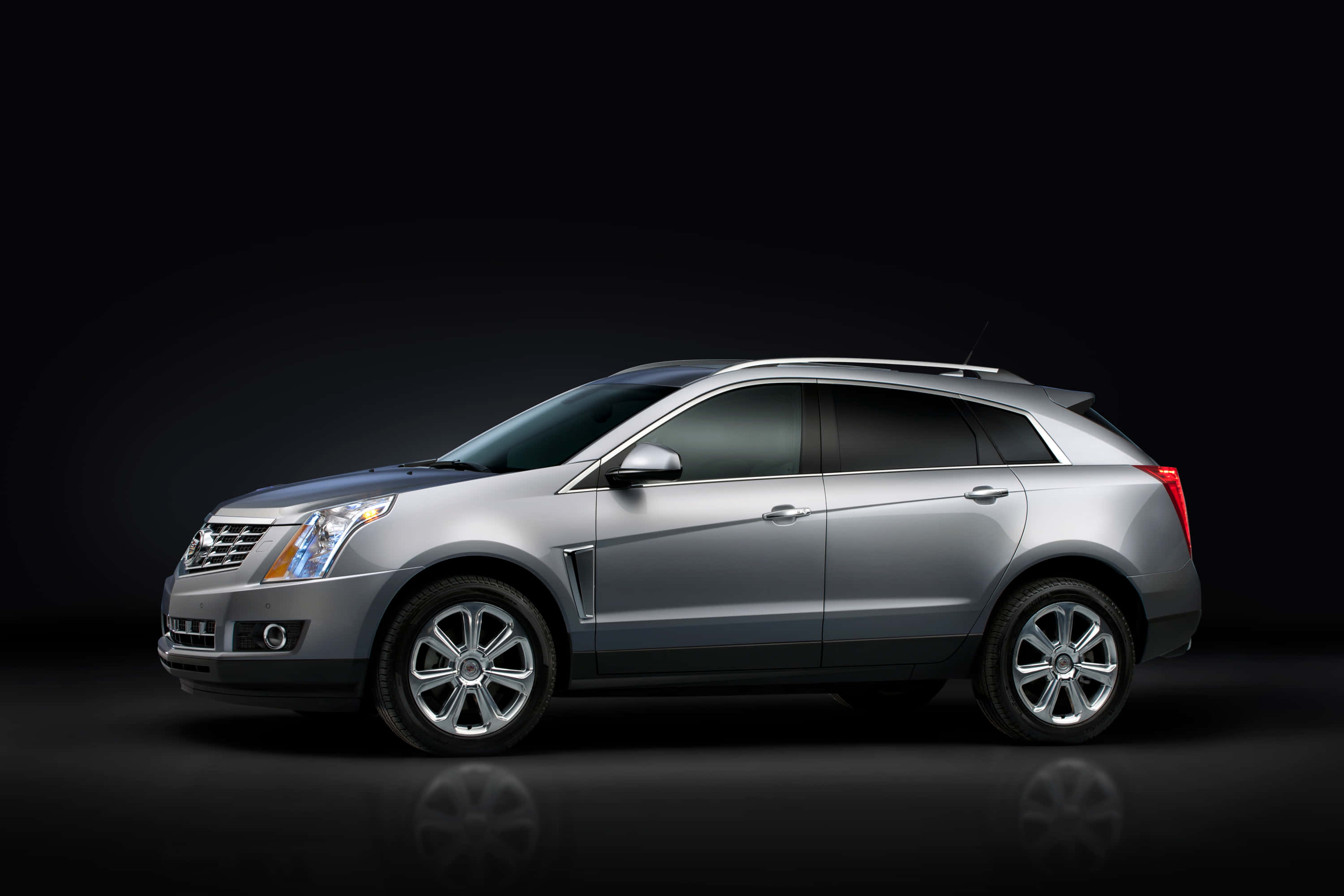 Cadillac Srx 桌布 壁紙 — 一輛時尚的銀色凱迪拉克SUV在黑暗的攝影棚中展示，配有反射地板和戲劇性燈光。