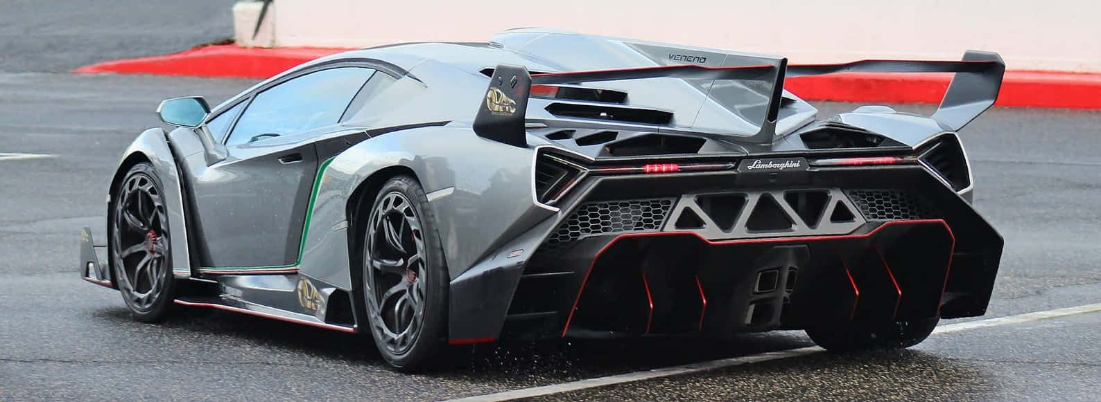 Lamborghini Veneno 桌布 壁紙 — 一架時尚的銀色林寶堅尼跑車，帶有紅色點綴和大型尾翼，停泊在潮濕的賽道上。
