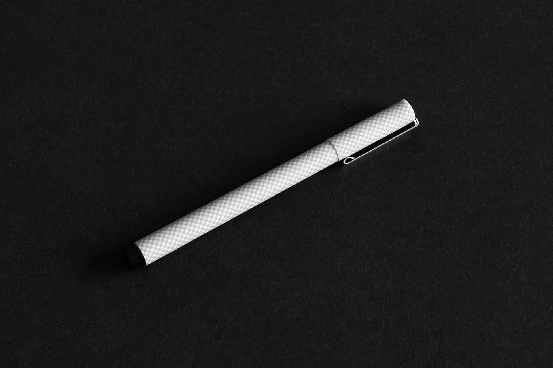  壁紙 — 一支帶有格紋質感的時尚銀色筆，在柔和的工作室燈光下斜放在磨砂黑色表面上。