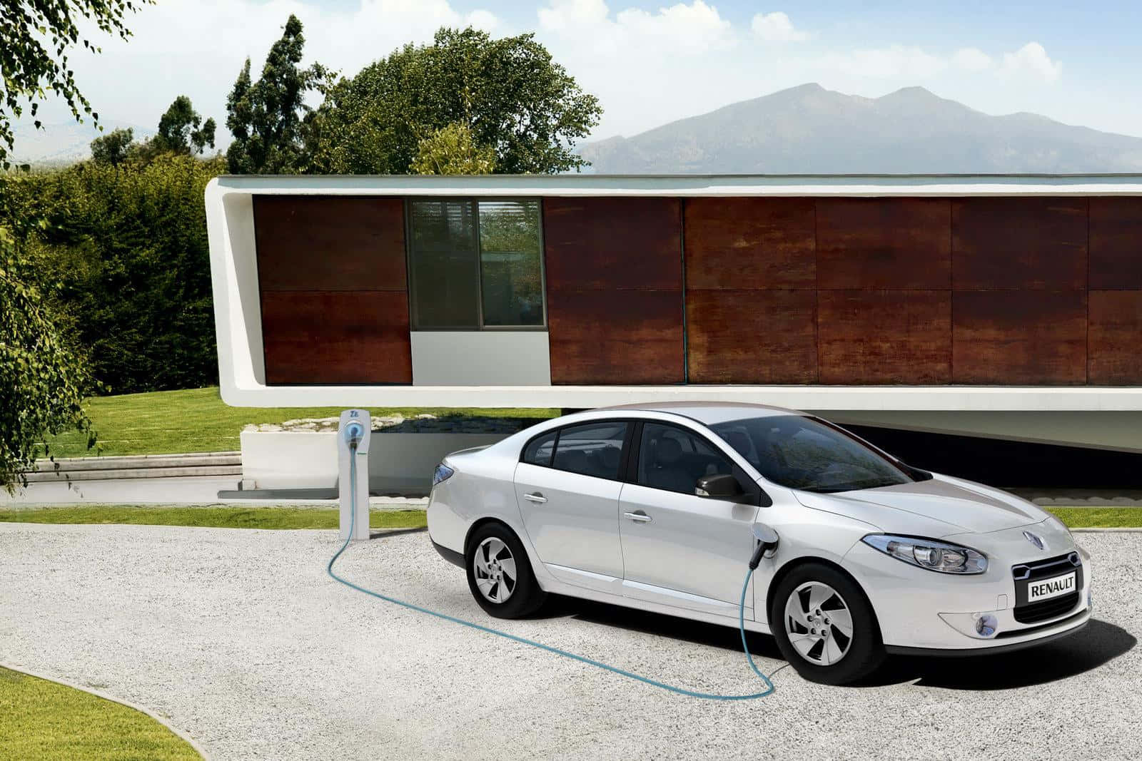 Renault Fluence 桌布 壁紙 — 一輛時尚的銀色雷諾轎車正在充電站充電，旁邊是一座現代木屋，背景有山巒。