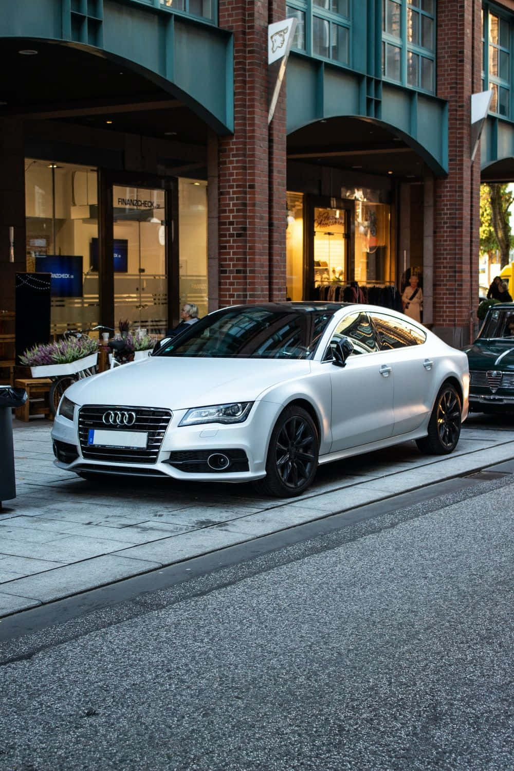 Audi A4 桌布 壁紙 — 一輛時尚的白色奧迪轎車配黑色輪圈，停泊在磚造建築和商店門面旁的城市街道上。