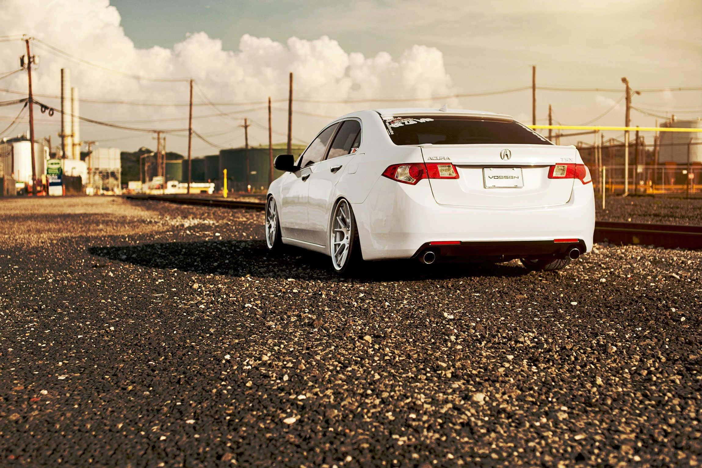 Acura Tsx 桌布 壁紙 — 一輛時尚的白色跑車停泊在工業區附近的碎石地上，天空多雲。