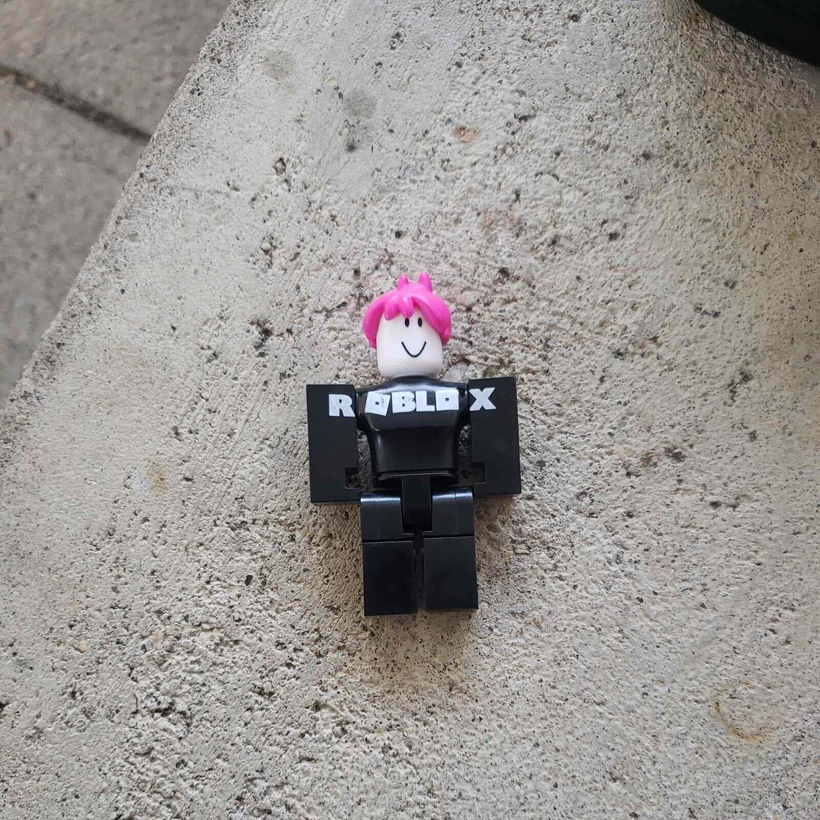  壁紙 — 一個細小的Roblox頭像公仔，粉紅色頭髮和黑色軀幹，坐在粗糙的混凝土表面上。