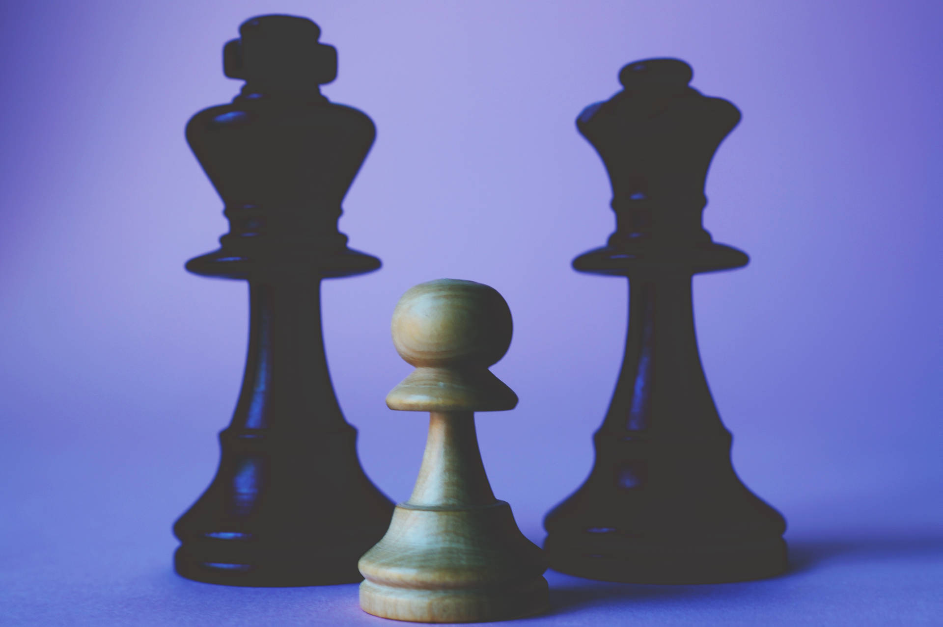 一個小棋兵在兩個大國王棋子之間，紫色表面上。