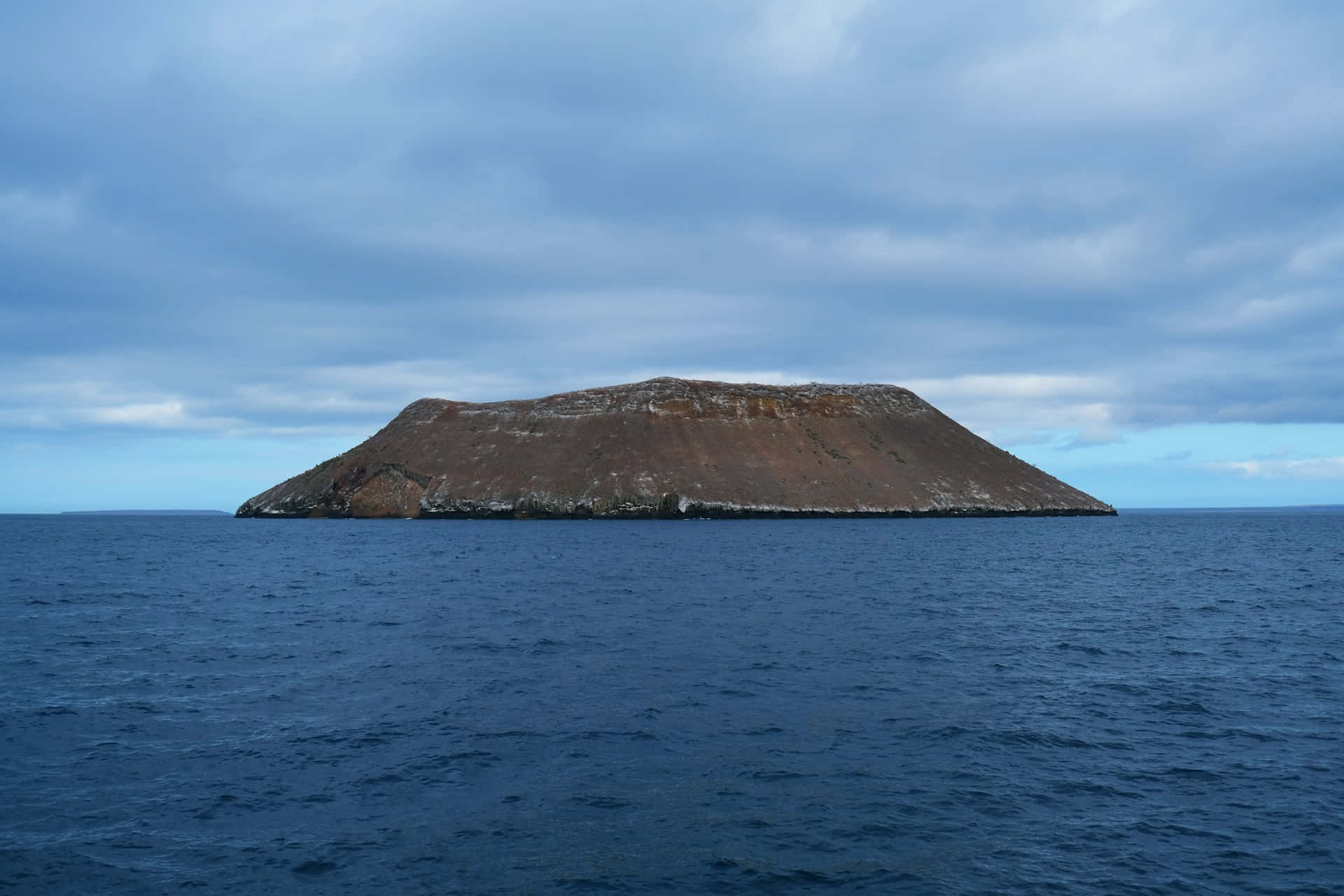  壁紙 — 一座孤獨的火山島從深藍色的海洋中升起，天空多雲。