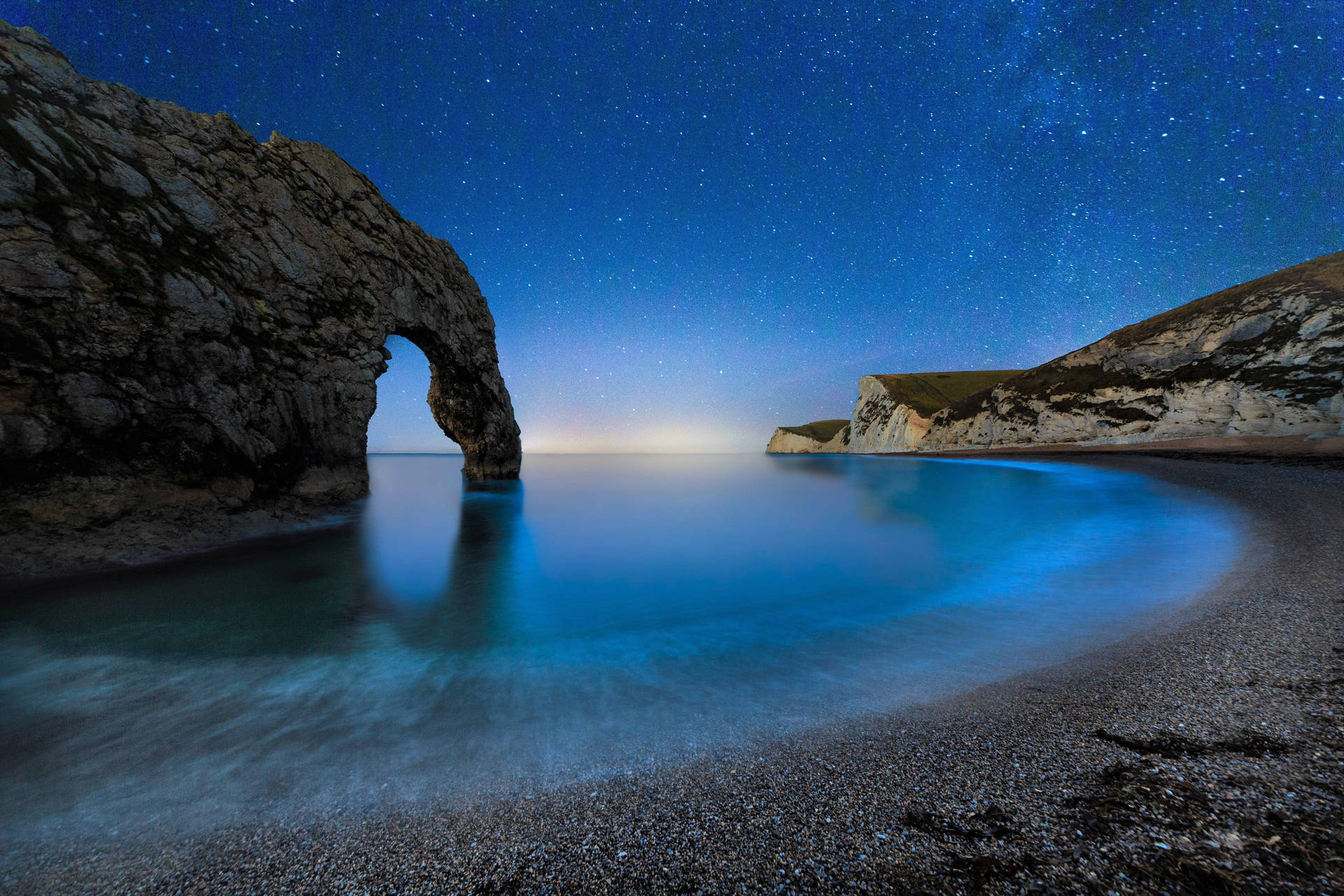 杜德爾門岩石拱門在星空夜空下，平靜的藍色海水。