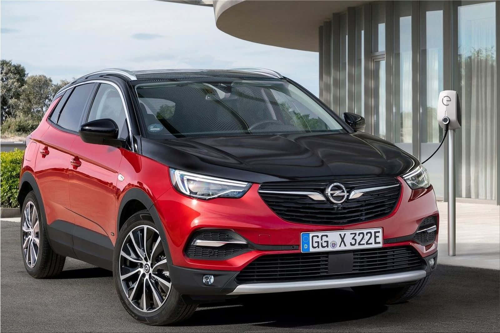 Opel Grandland X 桌布 壁紙 — 一輛搶眼的紅黑色Opel電動SUV在晴朗天空下的現代充電站充電。