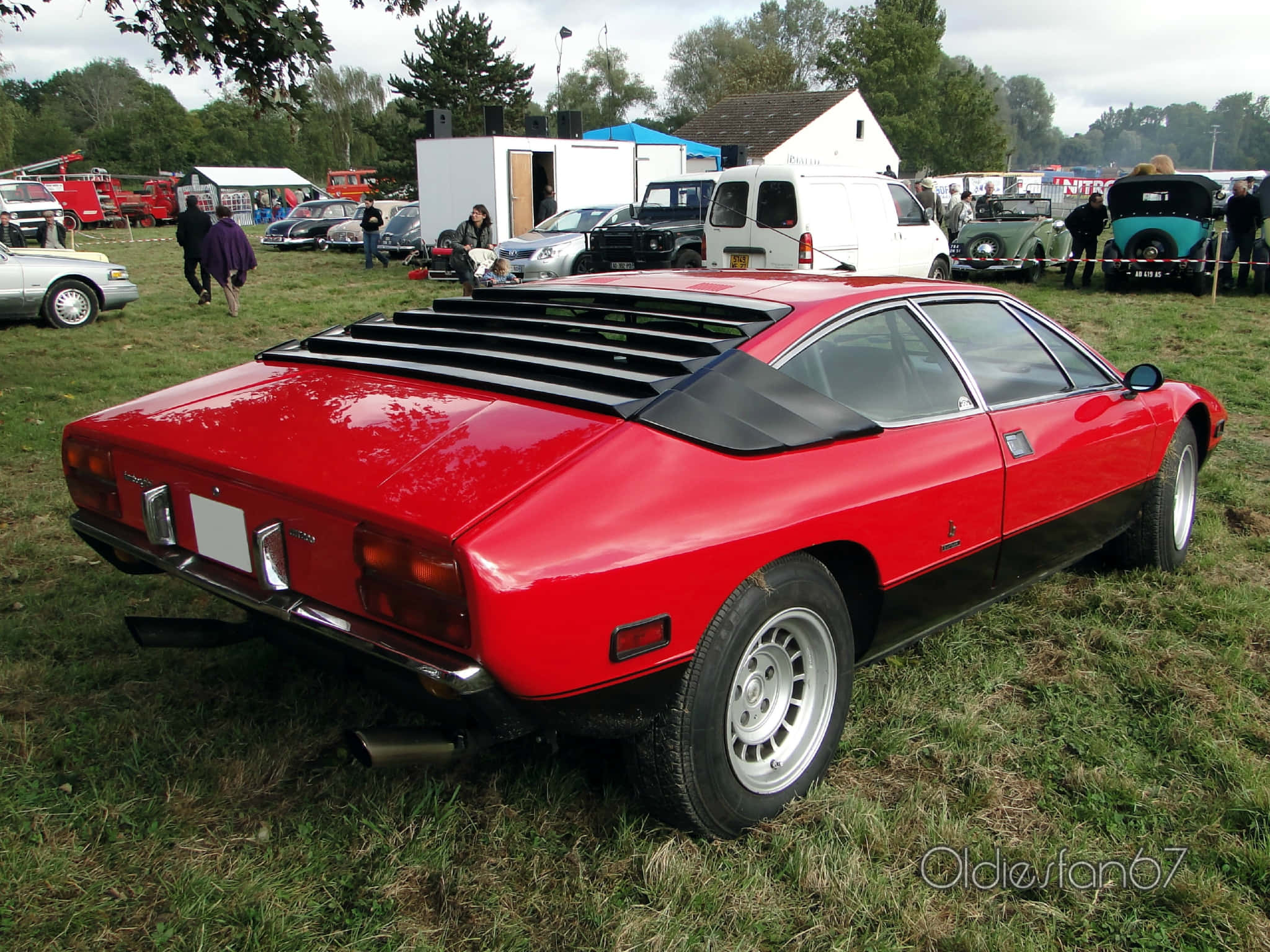 Lamborghini Urraco 桌布 壁紙 — 一輛引人注目的紅黑復古跑車，帶有車頂通風口，停在戶外經典車展的草地上。
