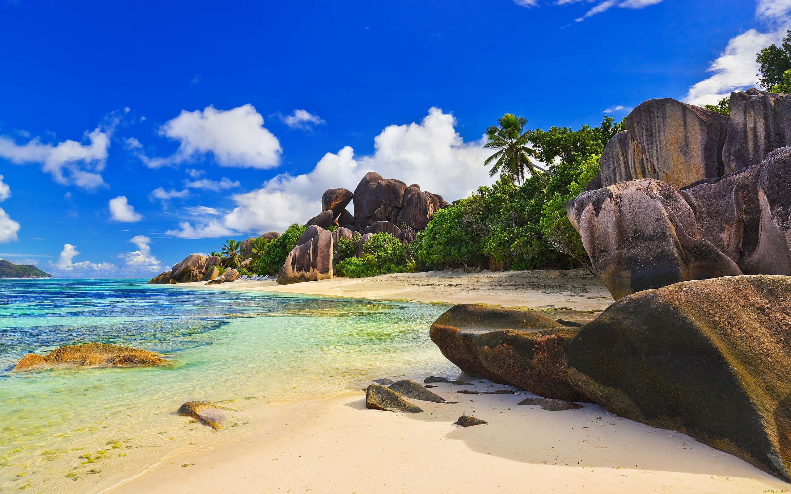 Beautiful Beach 桌布 壁紙 — 一個令人驚嘆的熱帶海灘，擁有碧綠的海水、白色的沙灘和巨大的花崗岩巨石，在明亮的藍天和蓬鬆的白雲下。