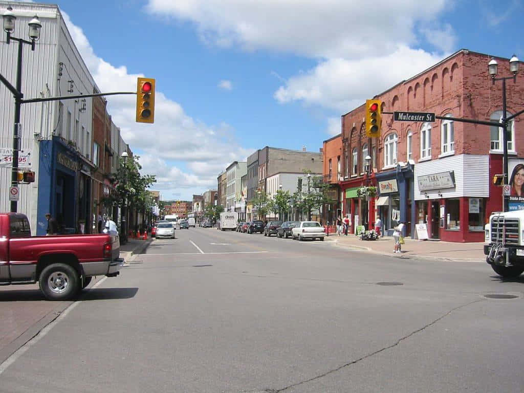 Barrie 桌布 壁紙 — 晴朗的一天，在寧靜的城市街道上，有磚砌建築、商店和汽車，藍天白雲。