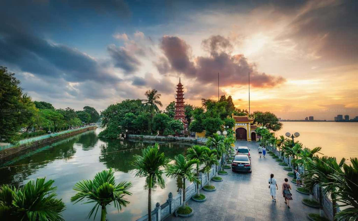 日落時分，湖中島上的寶塔，棕櫚樹和行人走在步道上。