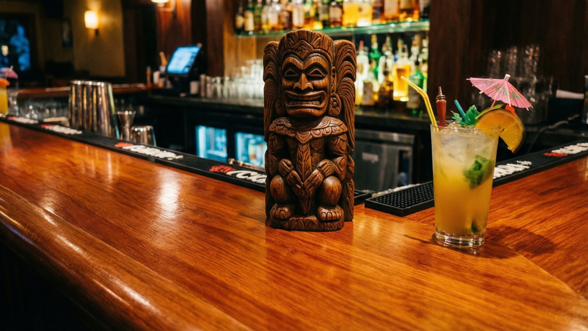 Tiki 桌布 壁紙 — 一個蒂基雕像和熱帶雞尾酒放在拋光木吧檯上，背後有發光的酒架。