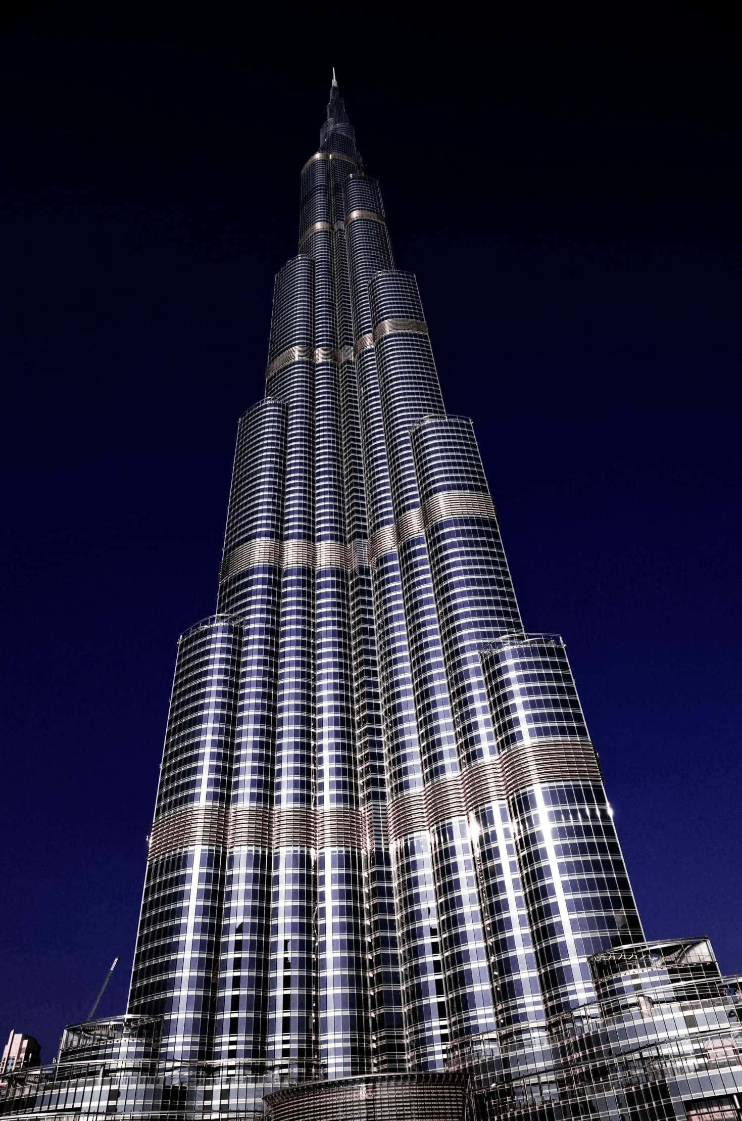 Burj Khalifa 桌布 壁紙 — 一座高聳的照明摩天大樓以其反光玻璃幕牆在黑暗中發光，刺穿深藍色的夜空。